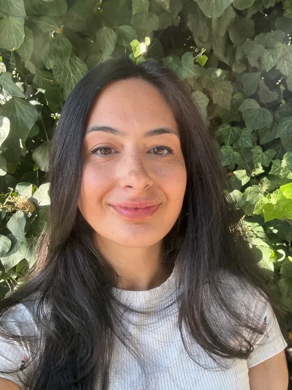 A headshot of Nell Winer, smiling in front of greenery.
