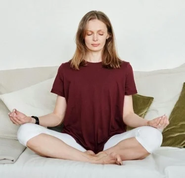A woman in a loose red shirt sitting with her eyes closed.