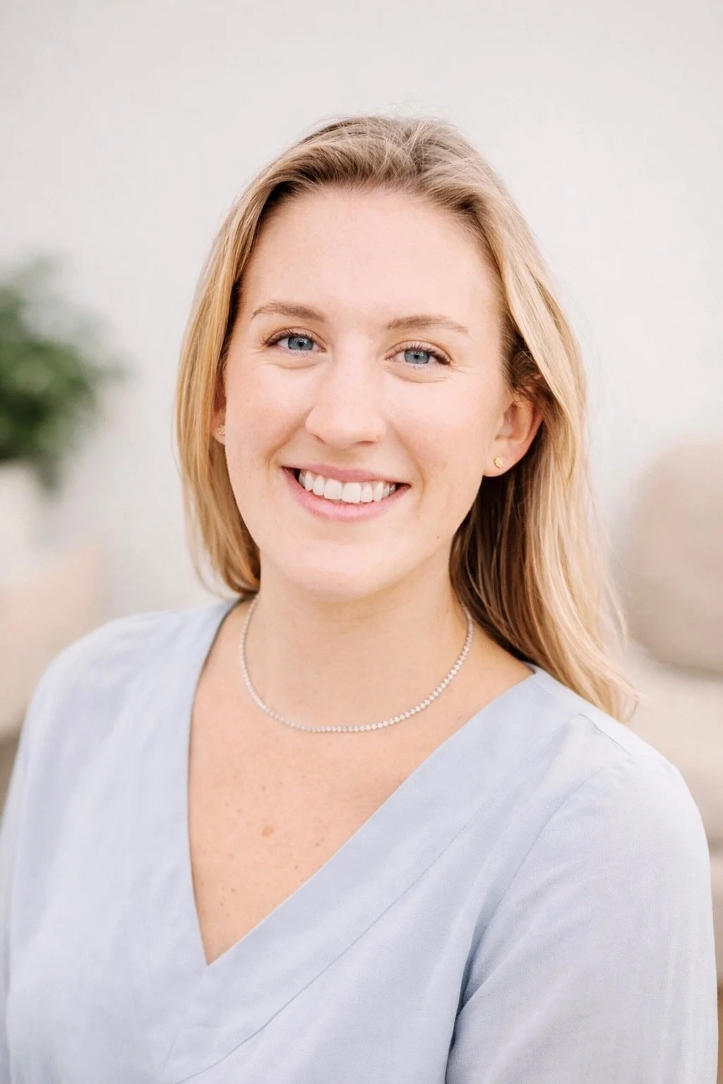 A woman with shoulder-length blonde hair smiling against a light green background.