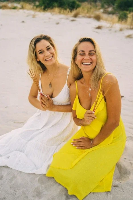 Two blonde women smiling on the beach.