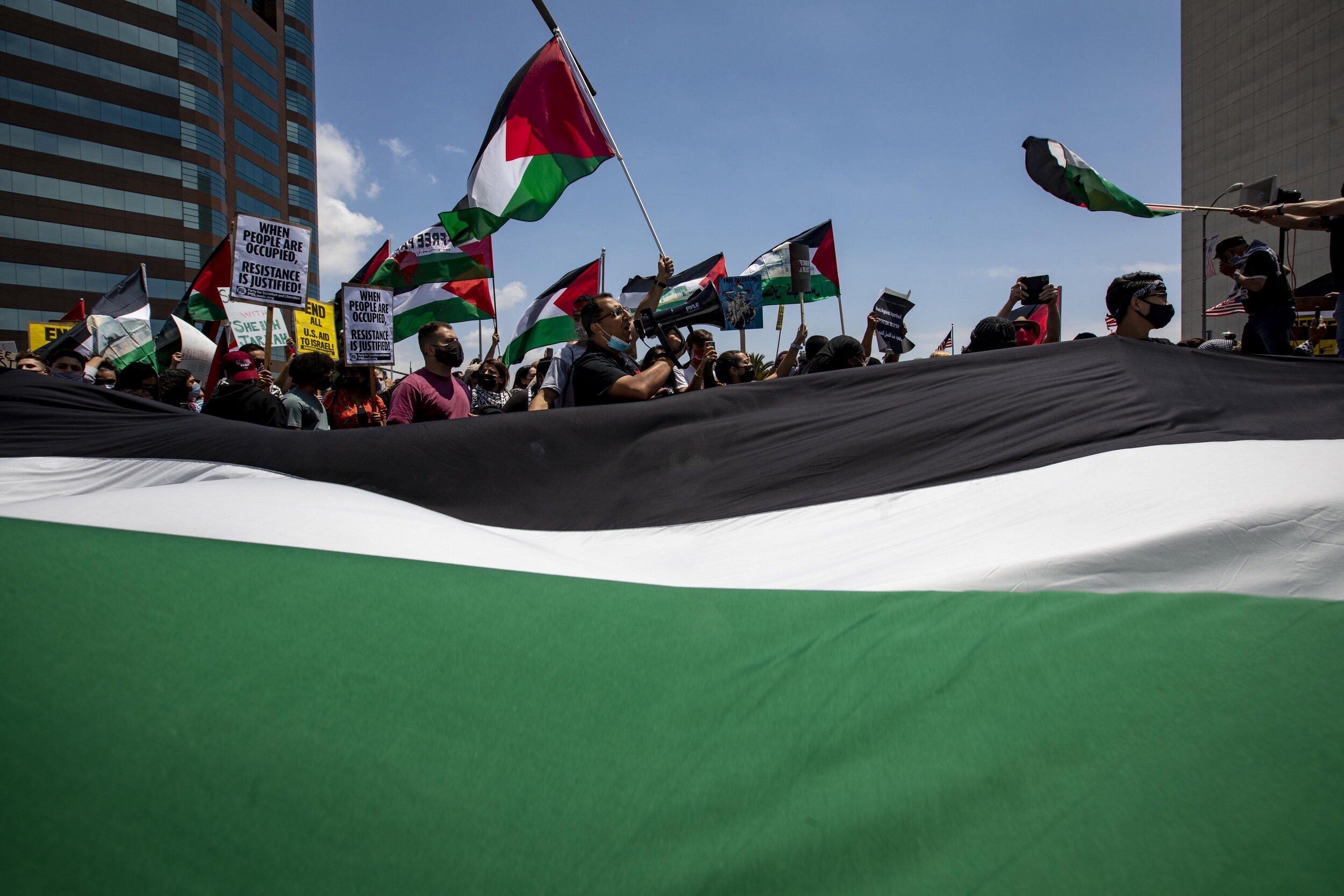  Protesters carry a giant Palestinian flag as they march along Wilshire Boulevard, which was closed down, to the Israeli Consulate General of Los Angeles. The march, which drew thousands,  was organized by the Palestine Youth movement.  
