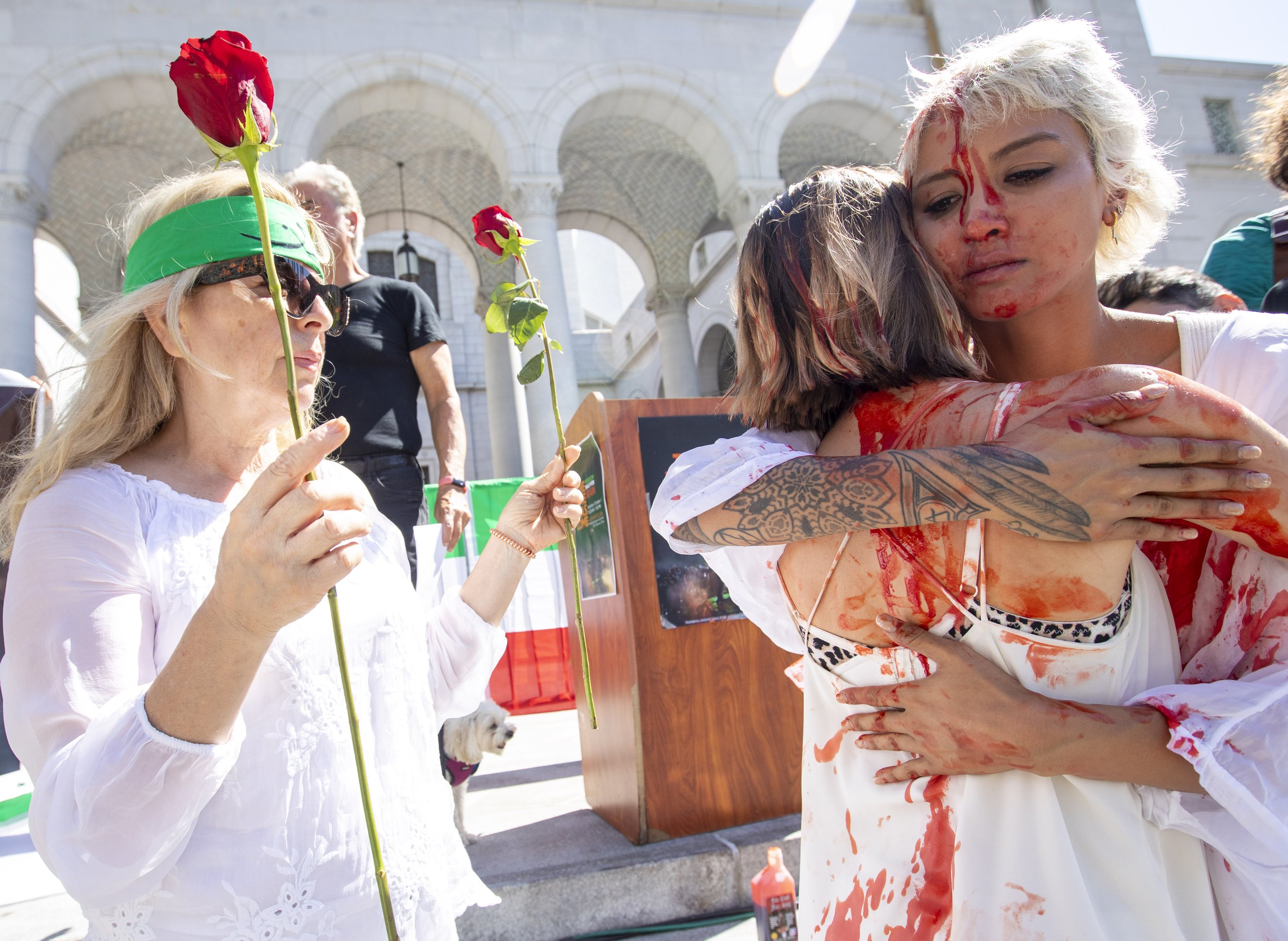  Artist Samantha Rose Moshiri  (right) hugs Yadriga Krasovskaya, as Nina Moyaer holds roses.  They are covered in fake blood from a performance in solidarity with Maha Amini outside City Hall  at a Freedom Rally for Iran in  Downtown Los Angeles, par
