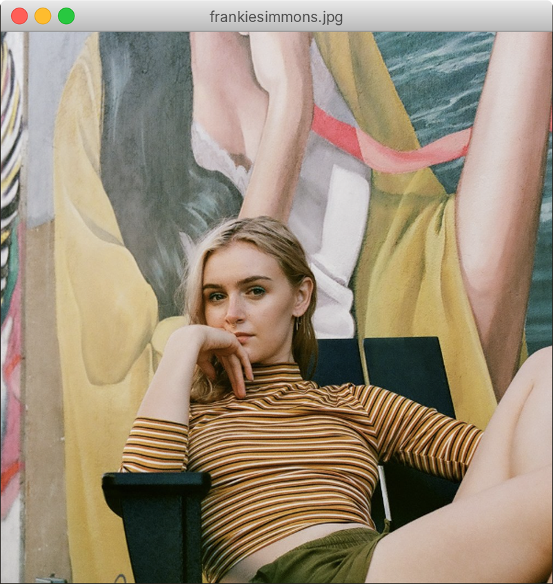 Frankie Simmons sitting in a chair in a striped top, resting her chin on her hand, in front of a painted mural