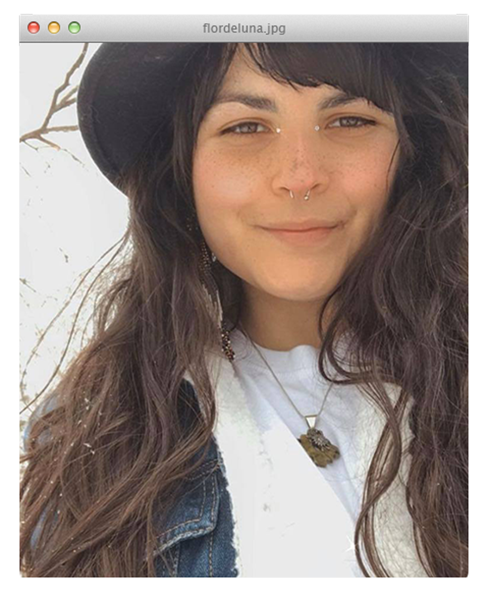 Flor De Luna smiling in a black hat and denim jacket with long dark hair
