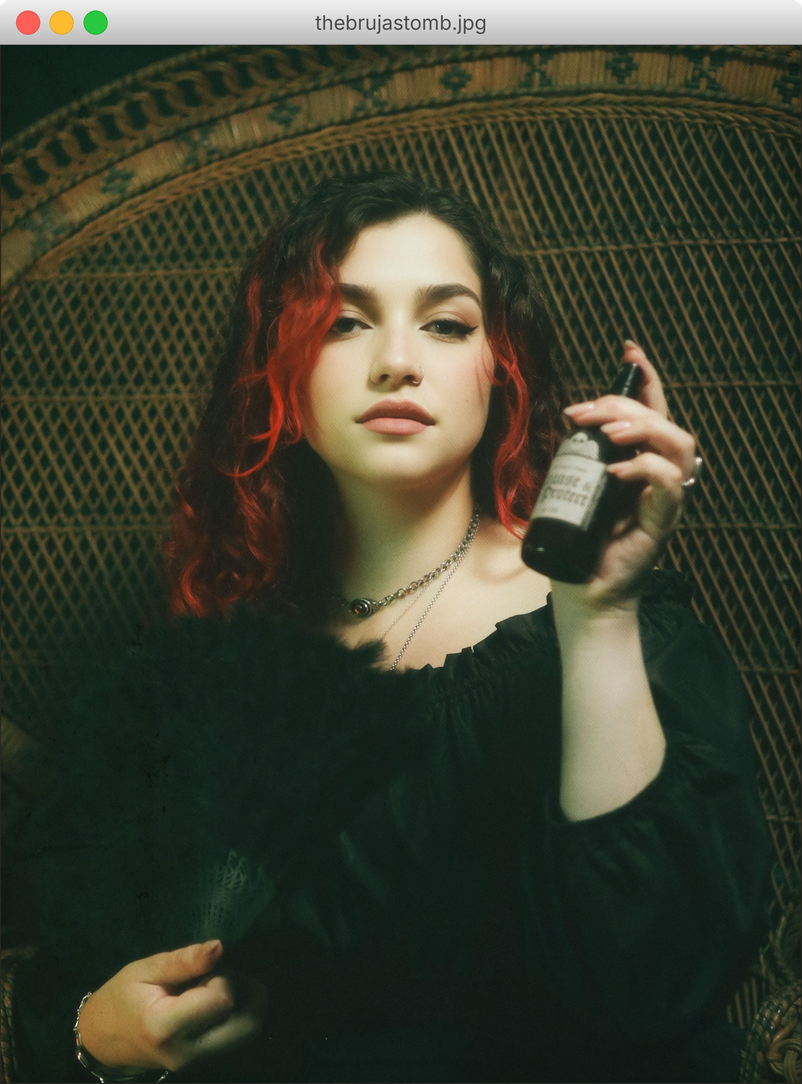Alexa Branco seated in a wicker peacock chair holding a bottle of her ritual spray