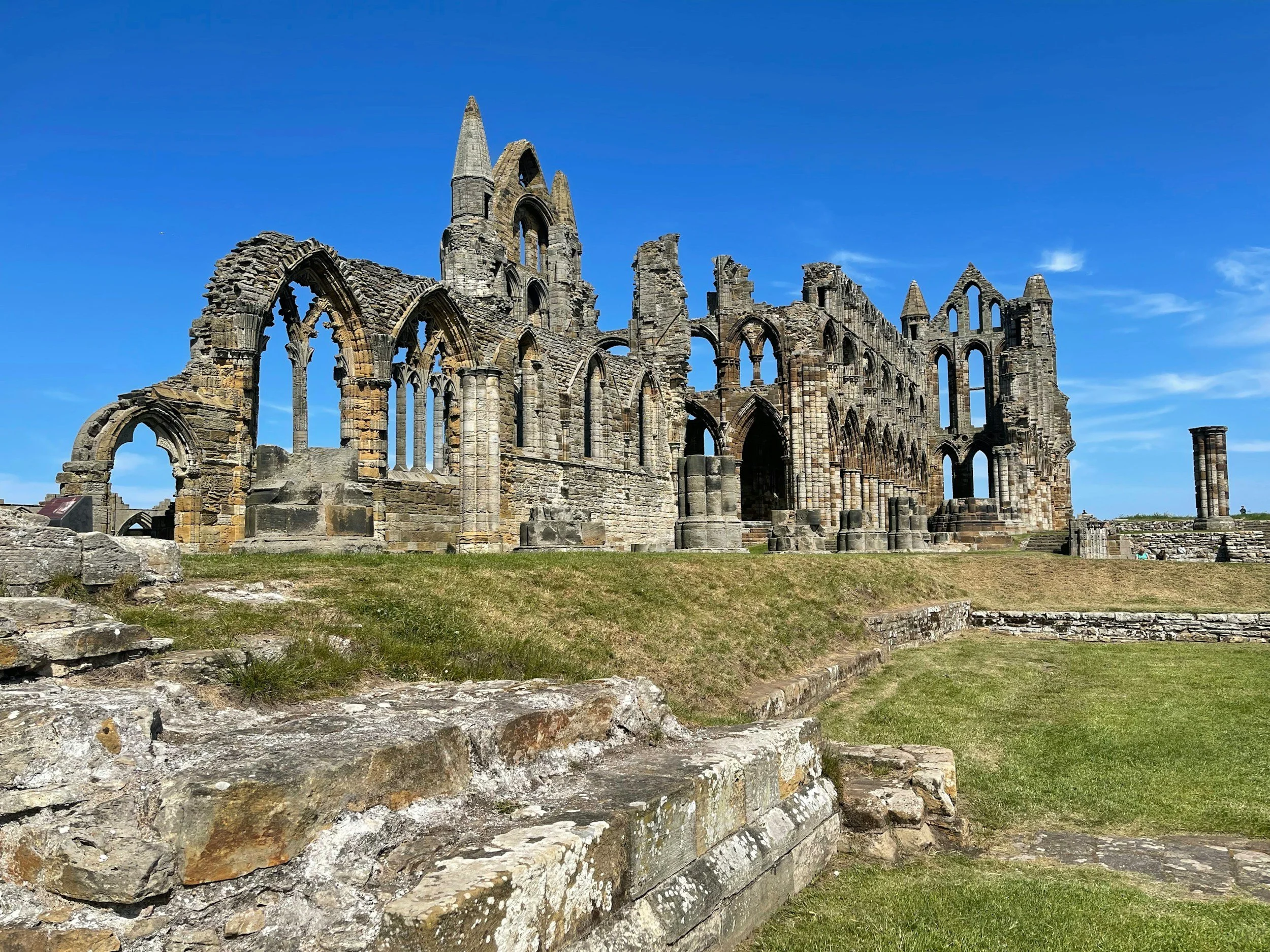 Ruins of an old stone church or abbey with tall, pointed windows and arches against a clear blue sky.