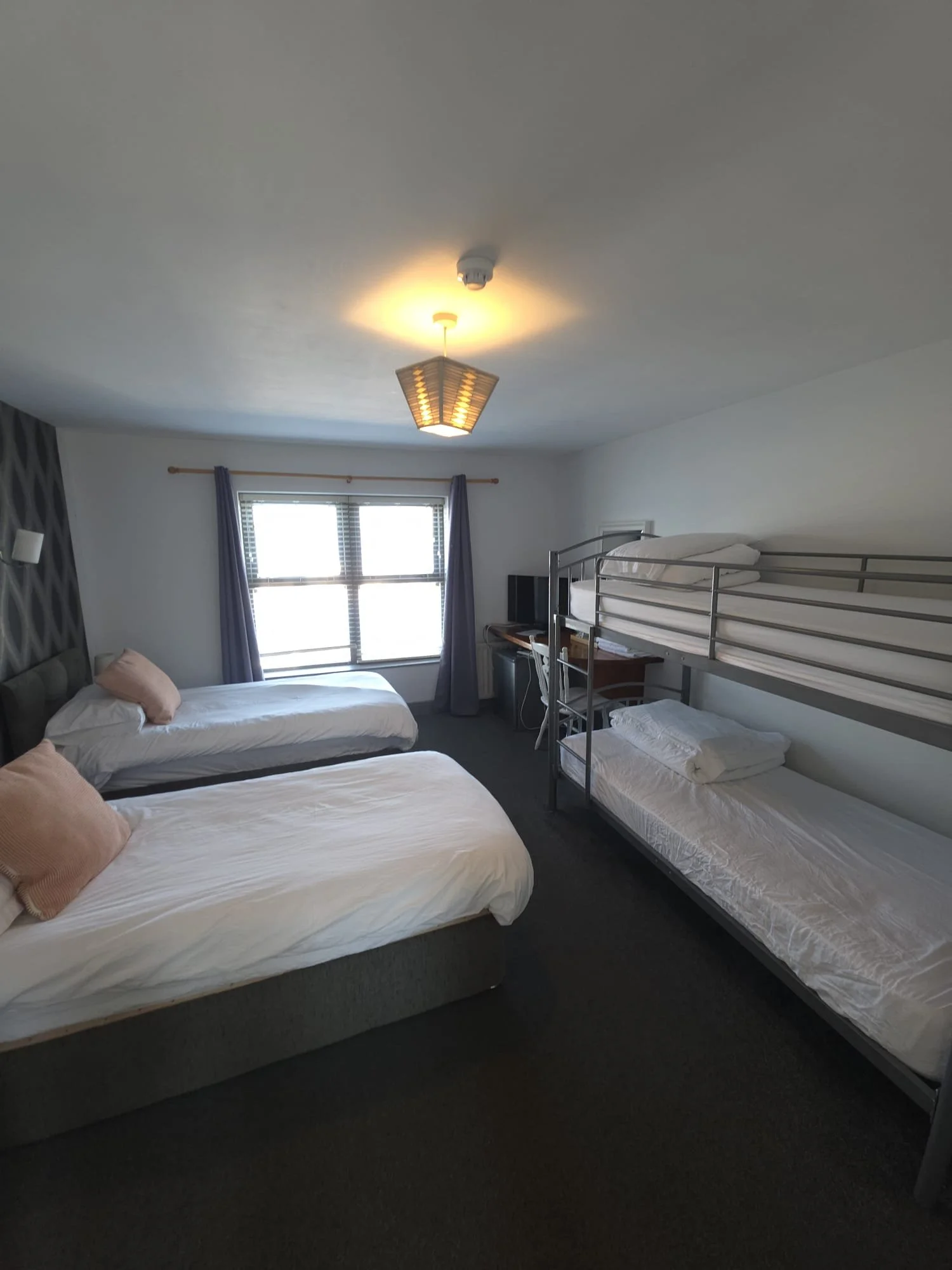 A bedroom with three beds, including a bunk bed and a mattress on the floor, a window with curtains, and a ceiling light fixture.