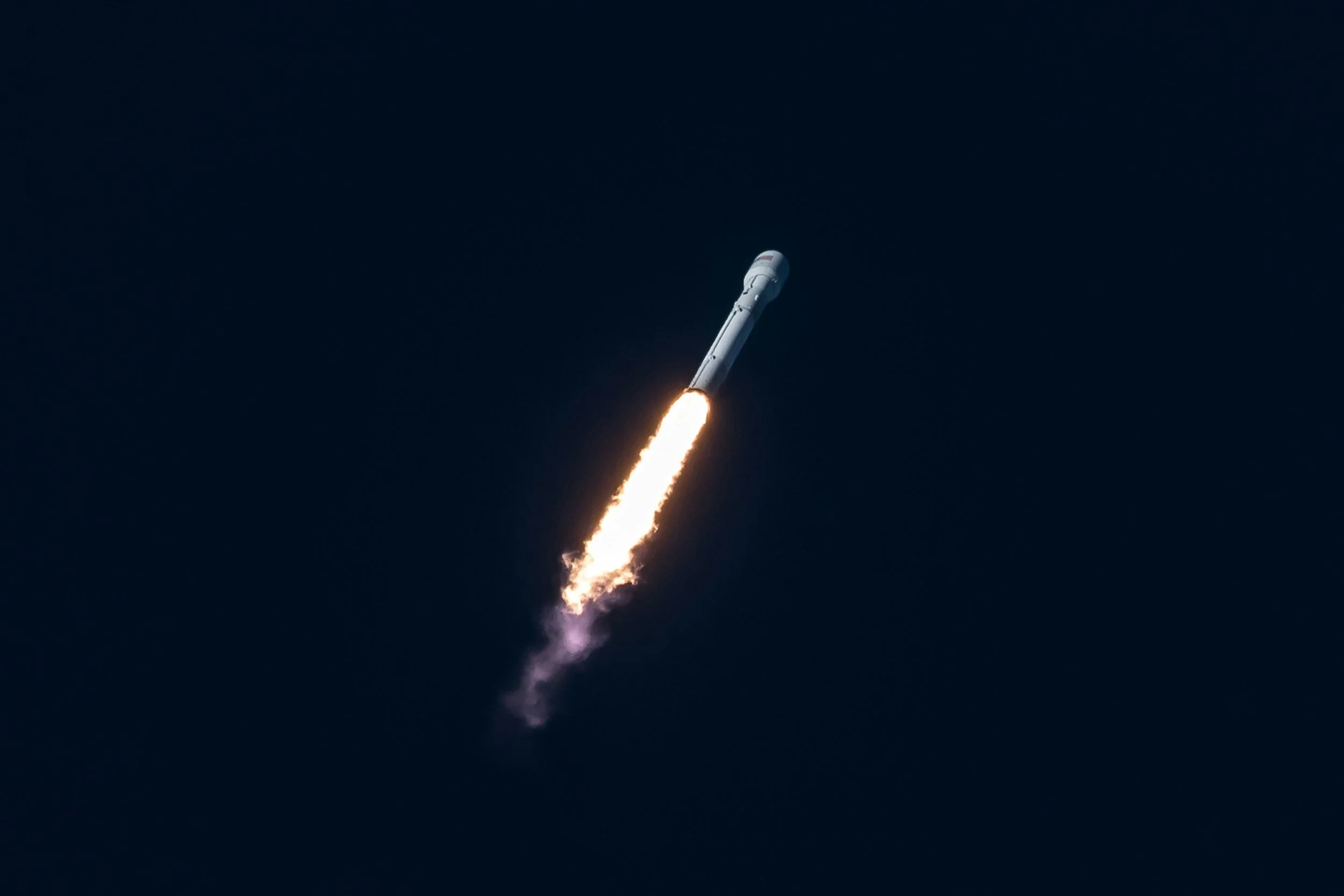 A rocket launching into space with a bright trail of flames and smoke against a dark sky.