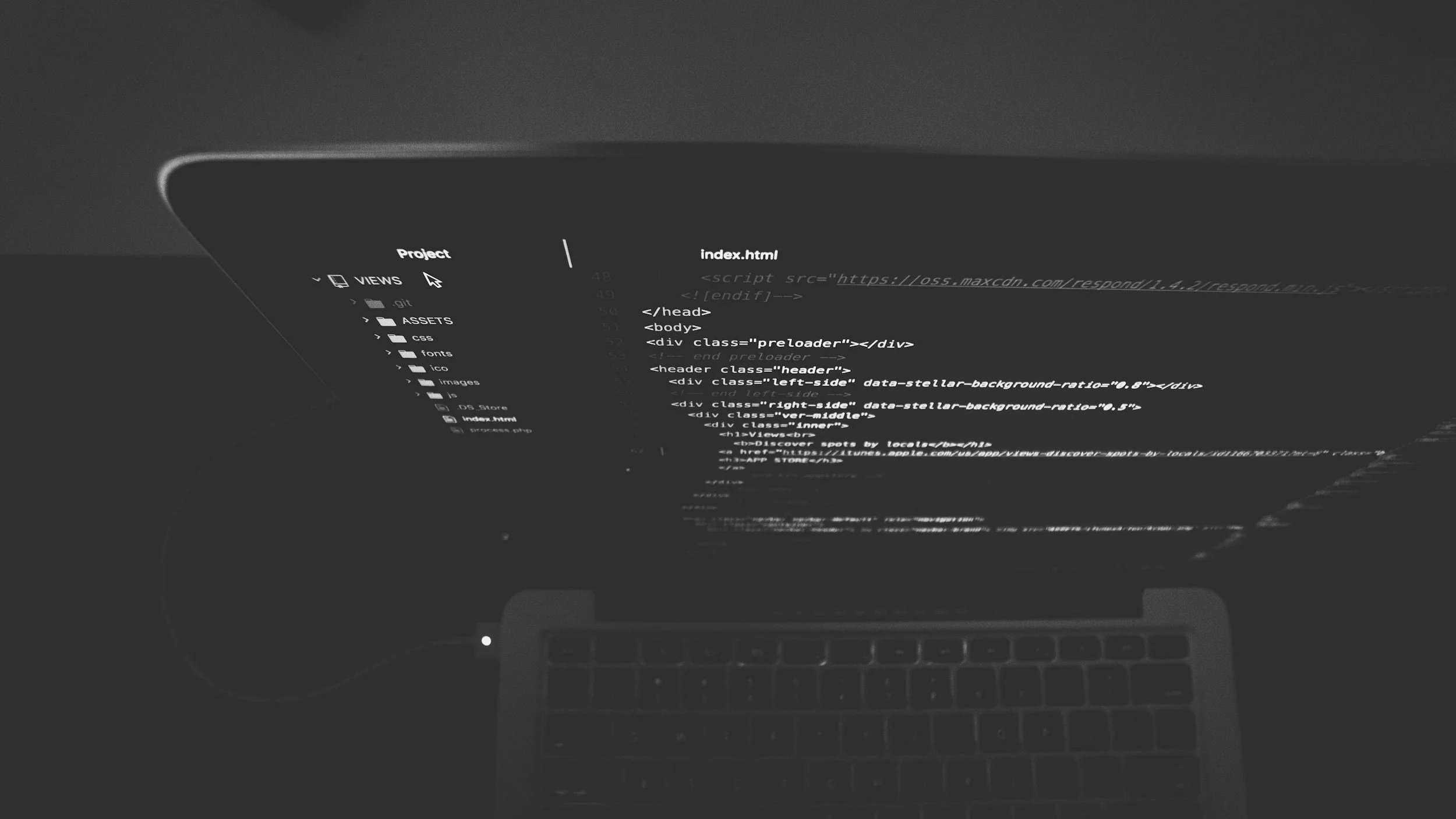 Laptop screen displaying a code editor with website HTML code visible, keyboard in foreground, dark grayscale setting.