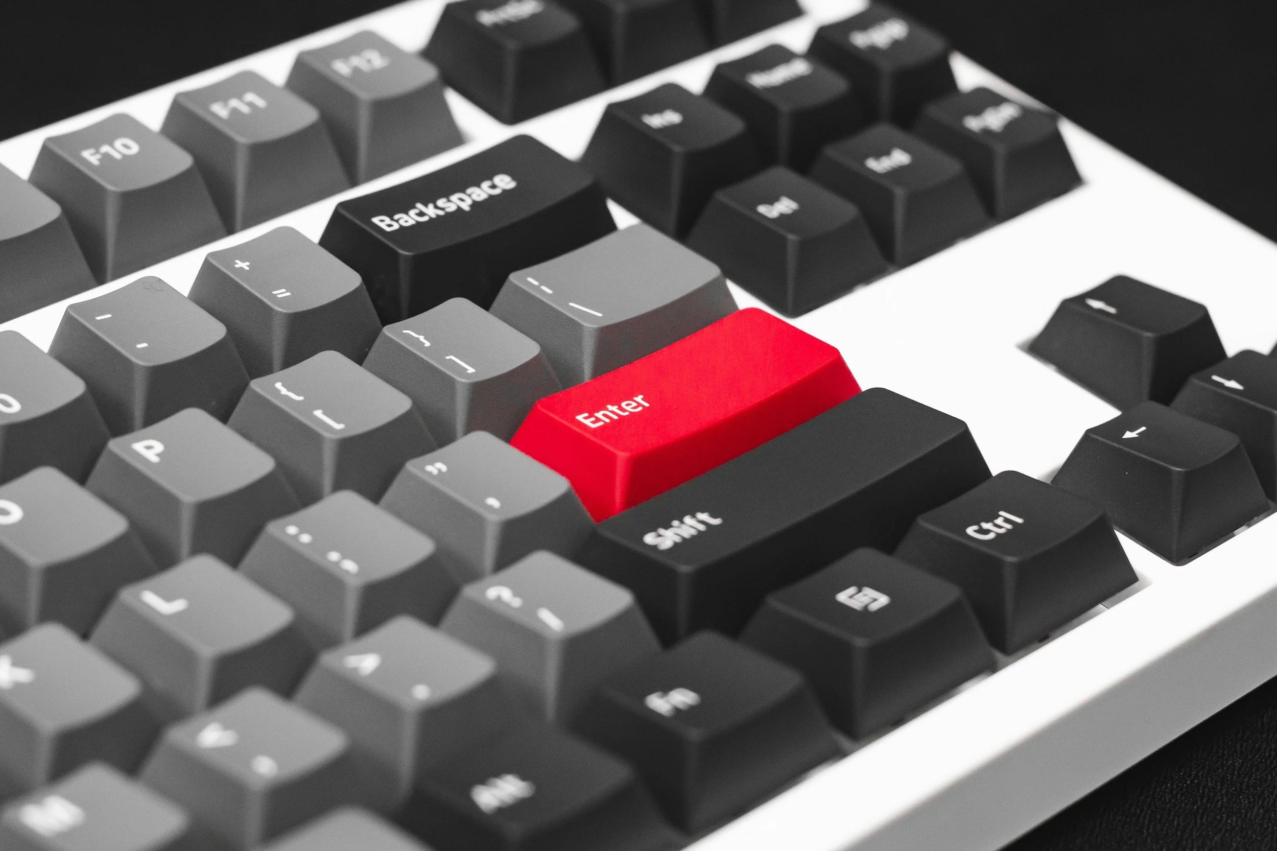 Close-up of a computer keyboard highlighting the red 'Enter' key among black and gray keys.