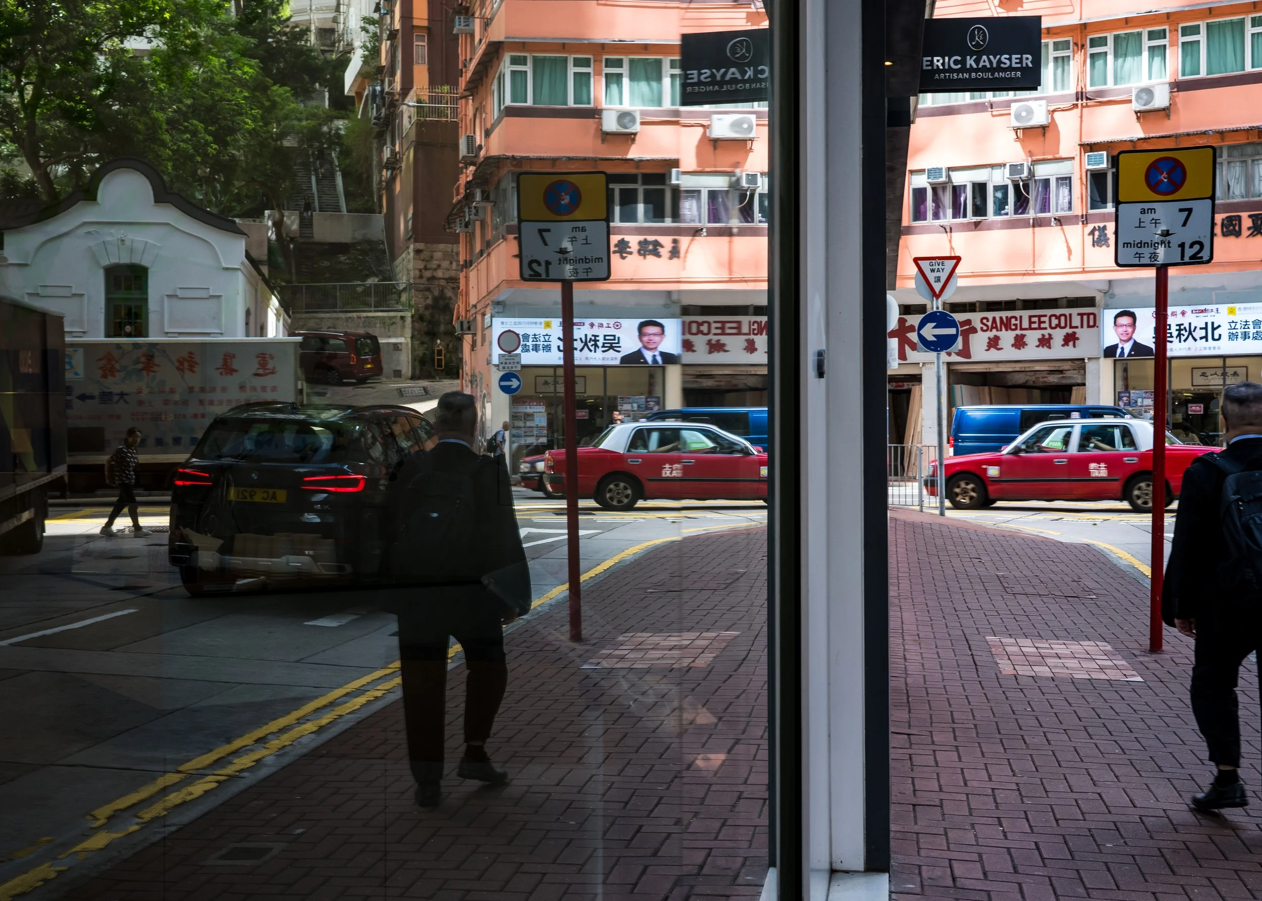 Man, cars and Taxi along with Shui Cheung Building reflected in Sunlight Tower windows.