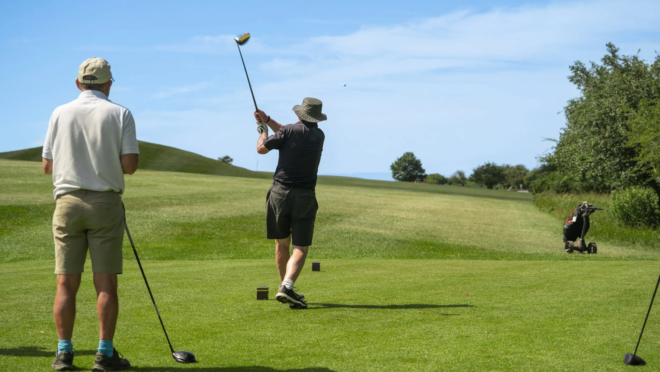 Male golfer swinging club with another golfer