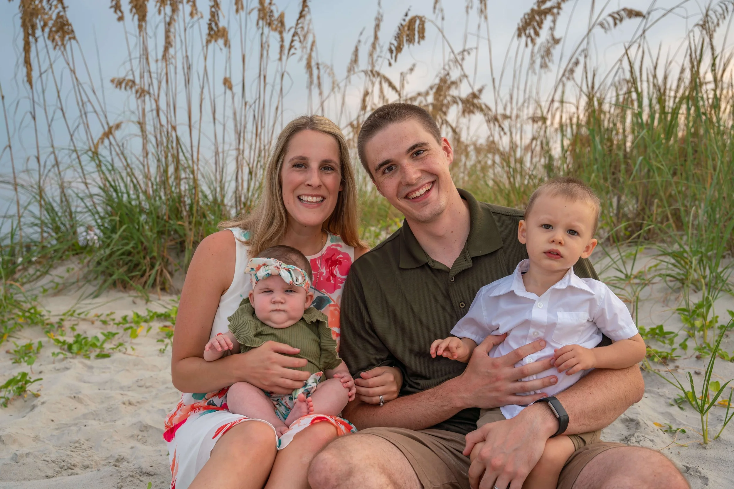 Young family of four sit on the beach, mom and dad are holding the young kids