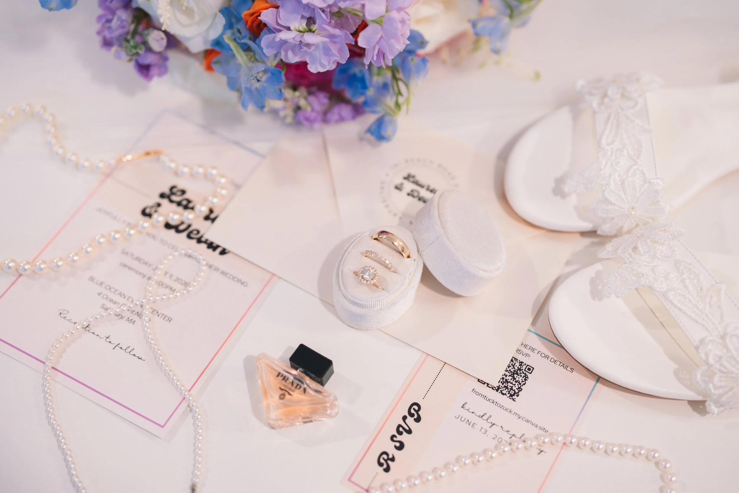 Wedding jewelry display with pearl necklaces, rings in white velvet boxes, and a floral bouquet in the background.