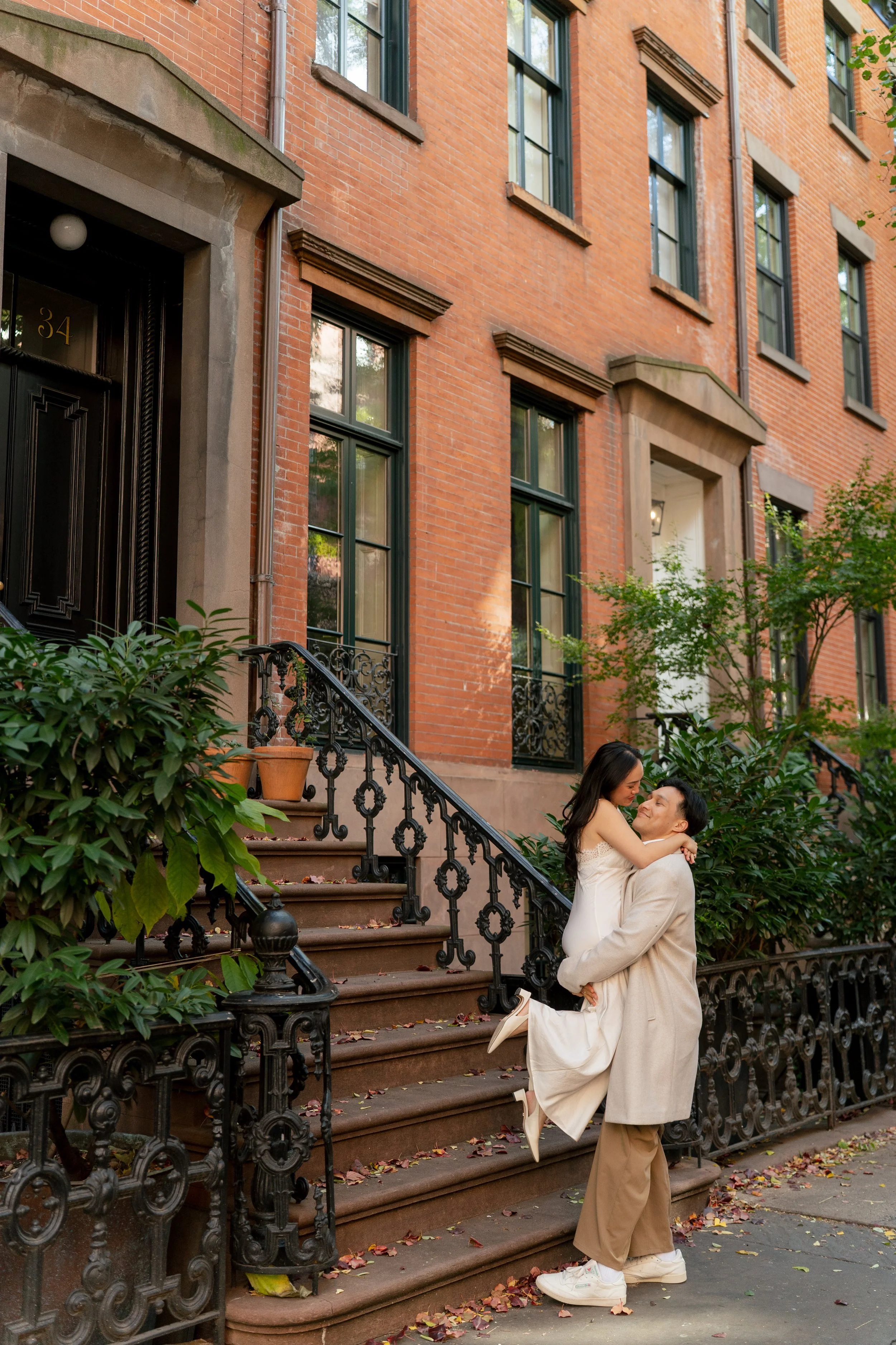 A couple hugging each other in front of the brownstones in West Village NYC for their NYC engagement session.
