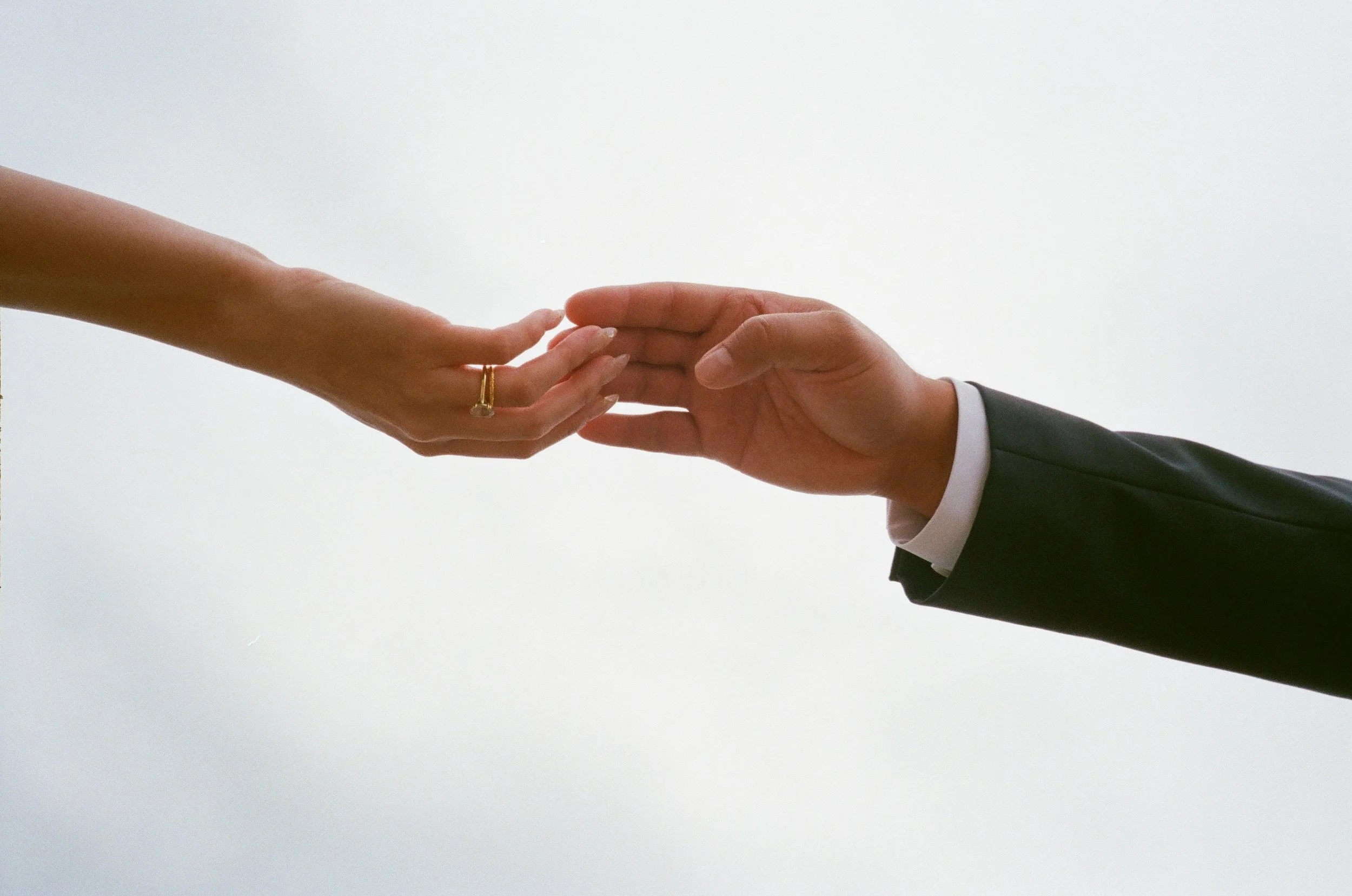 A person in a suit extending their hand to a woman, who is reaching out to shake hands, with a plain white background.