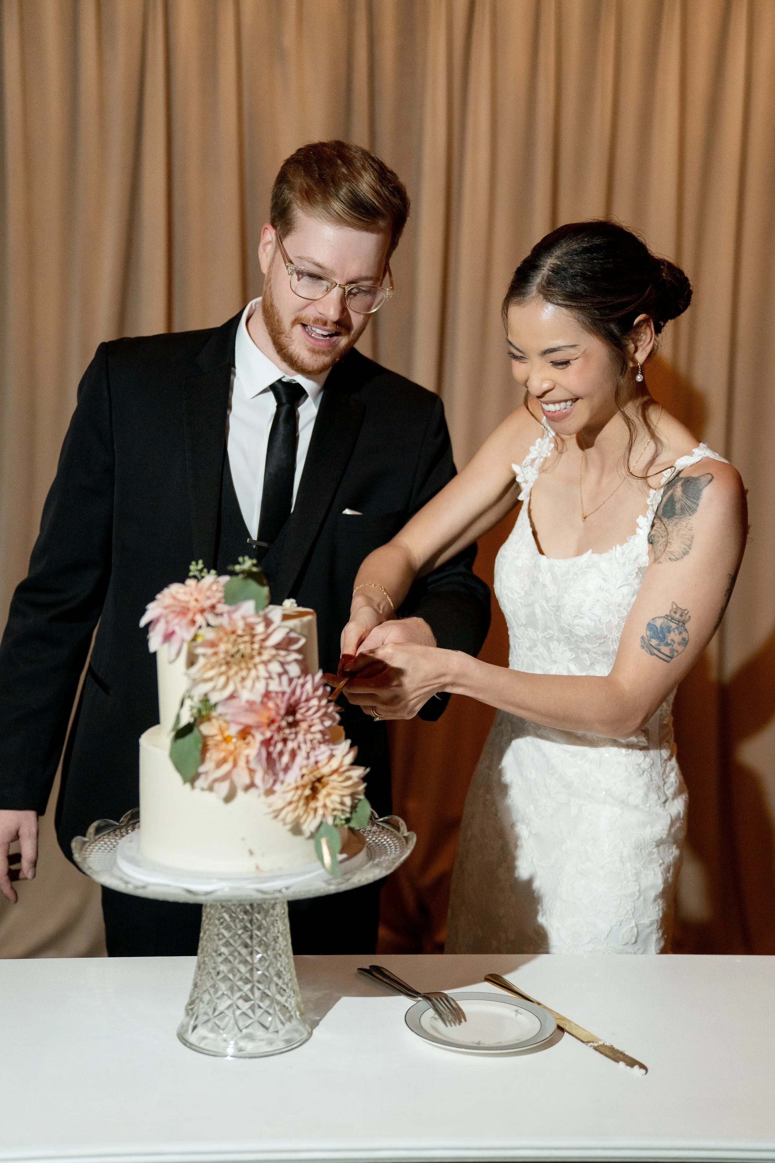 A bride and groom cutting a wedding cake together, smiling at each other.
