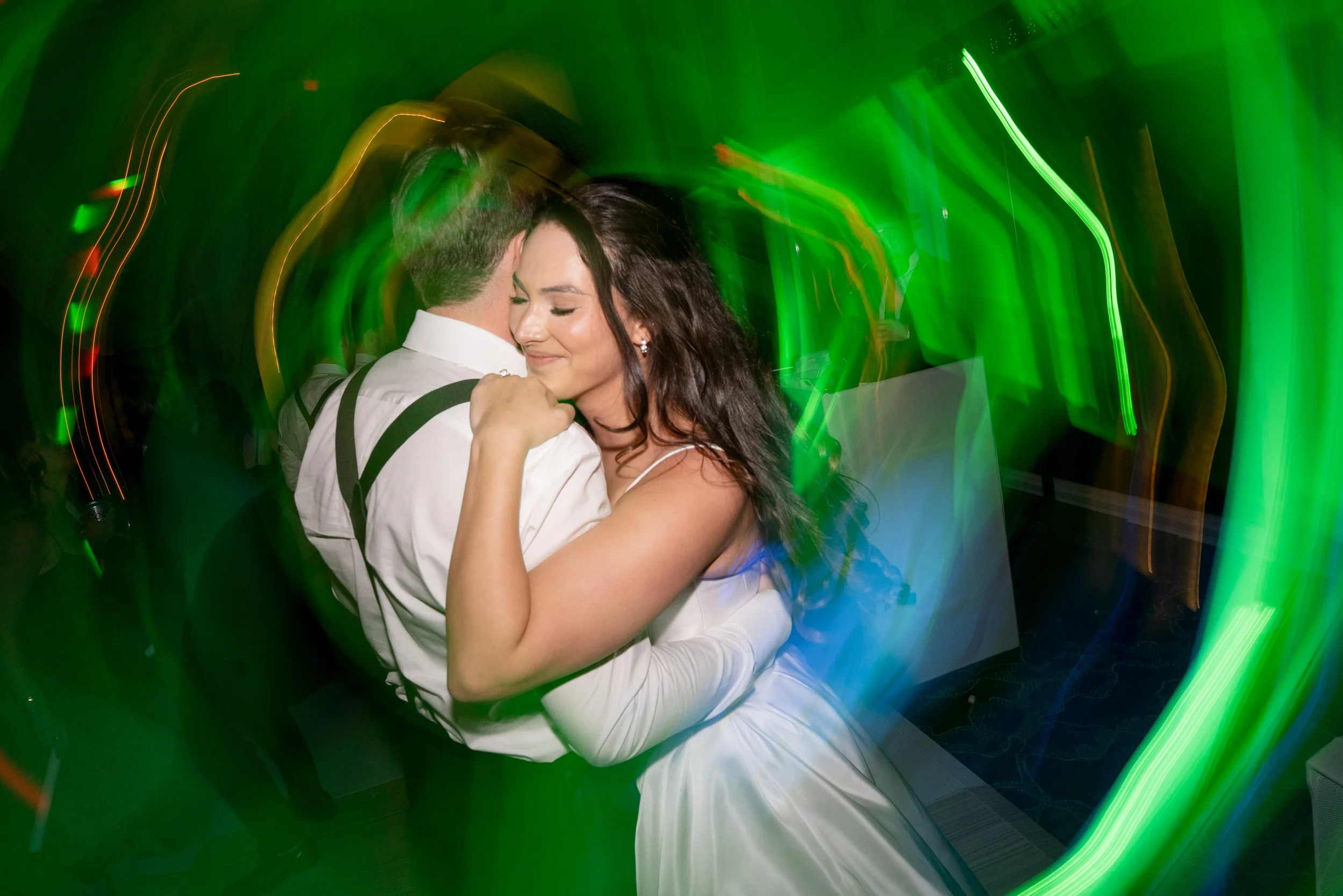 A couple dancing closely at a party with colorful lights and blurred motion.
