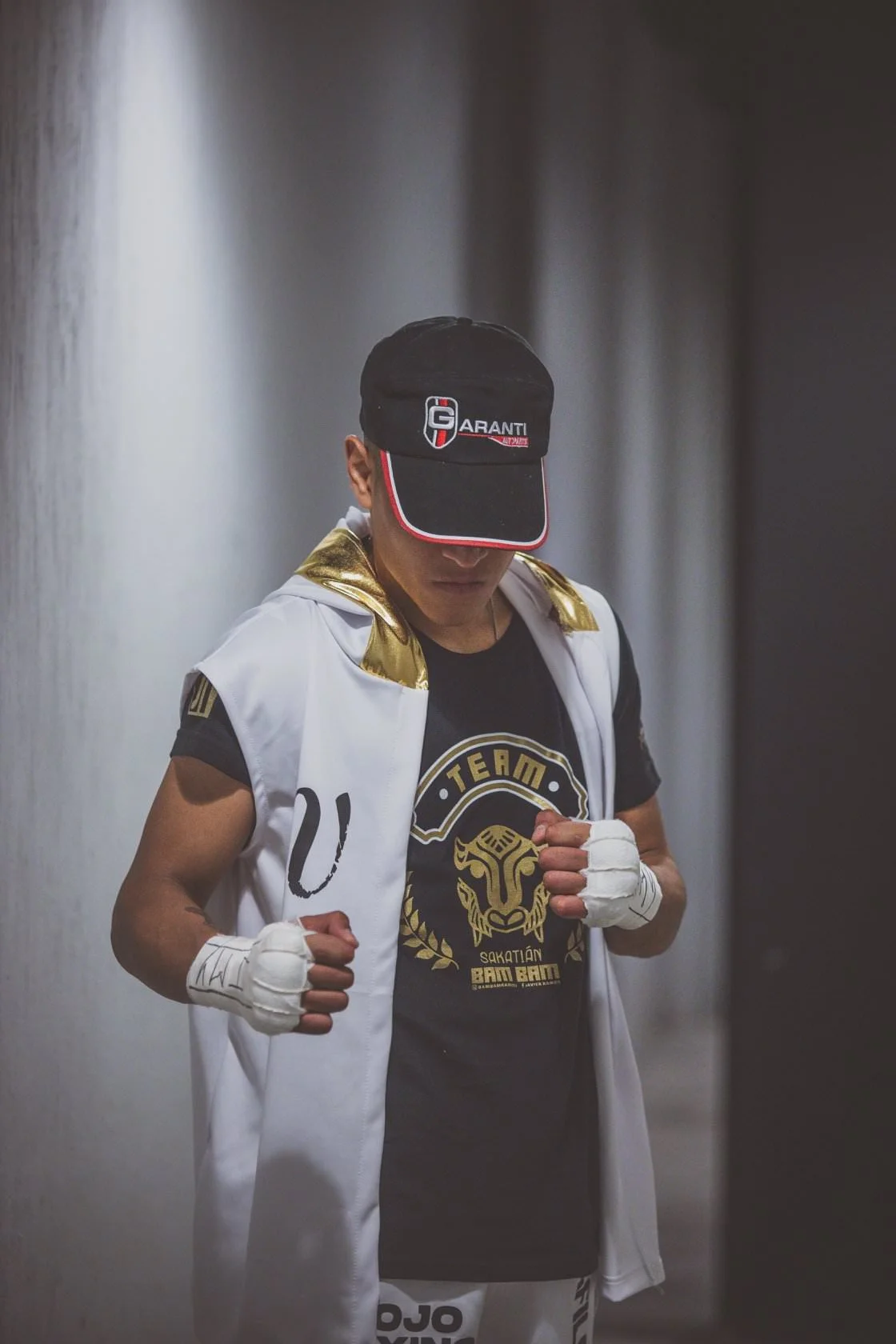Boxeador con gorra y guantes de vendaje, luciendo una camiseta negra con diseño de león, y capa blanca.