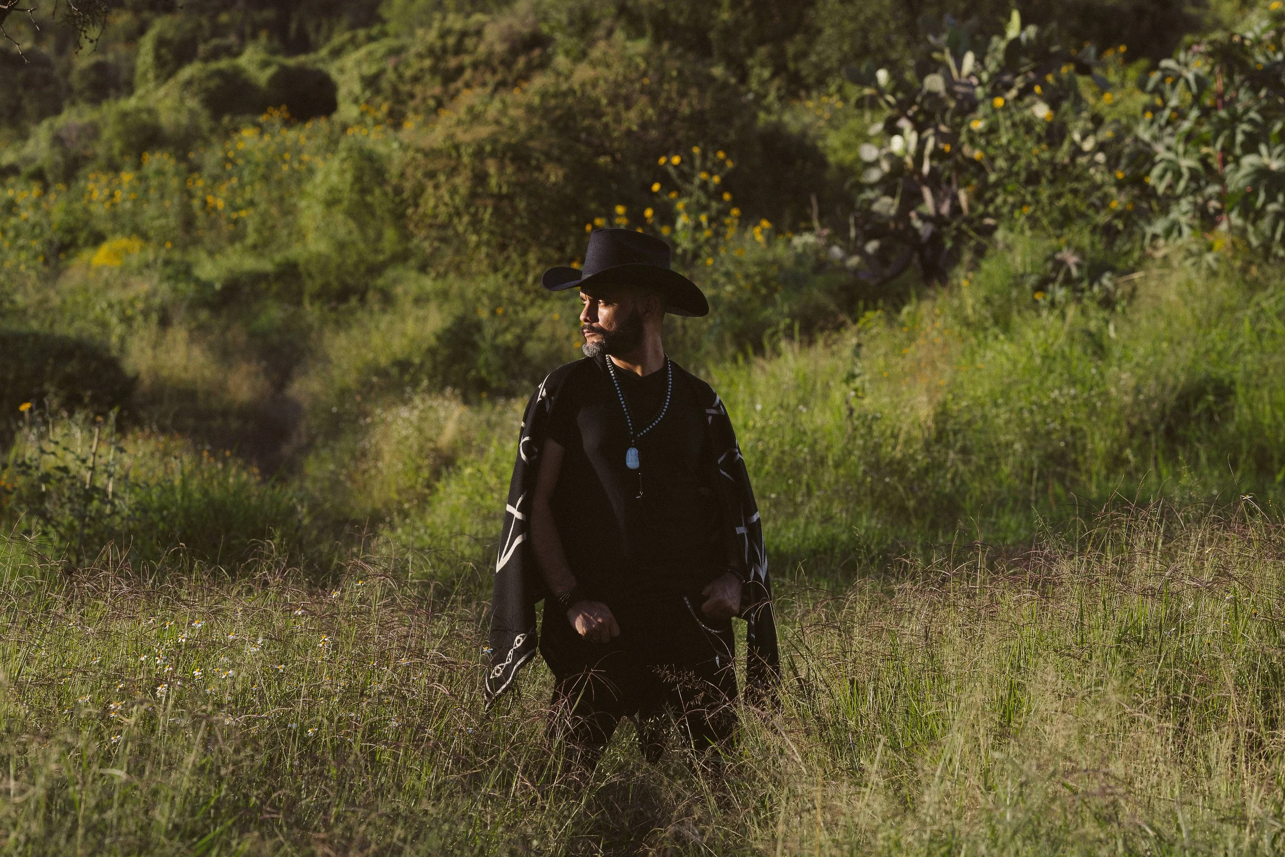 Hombre con sombrero negro y chaleco en un campo verde.