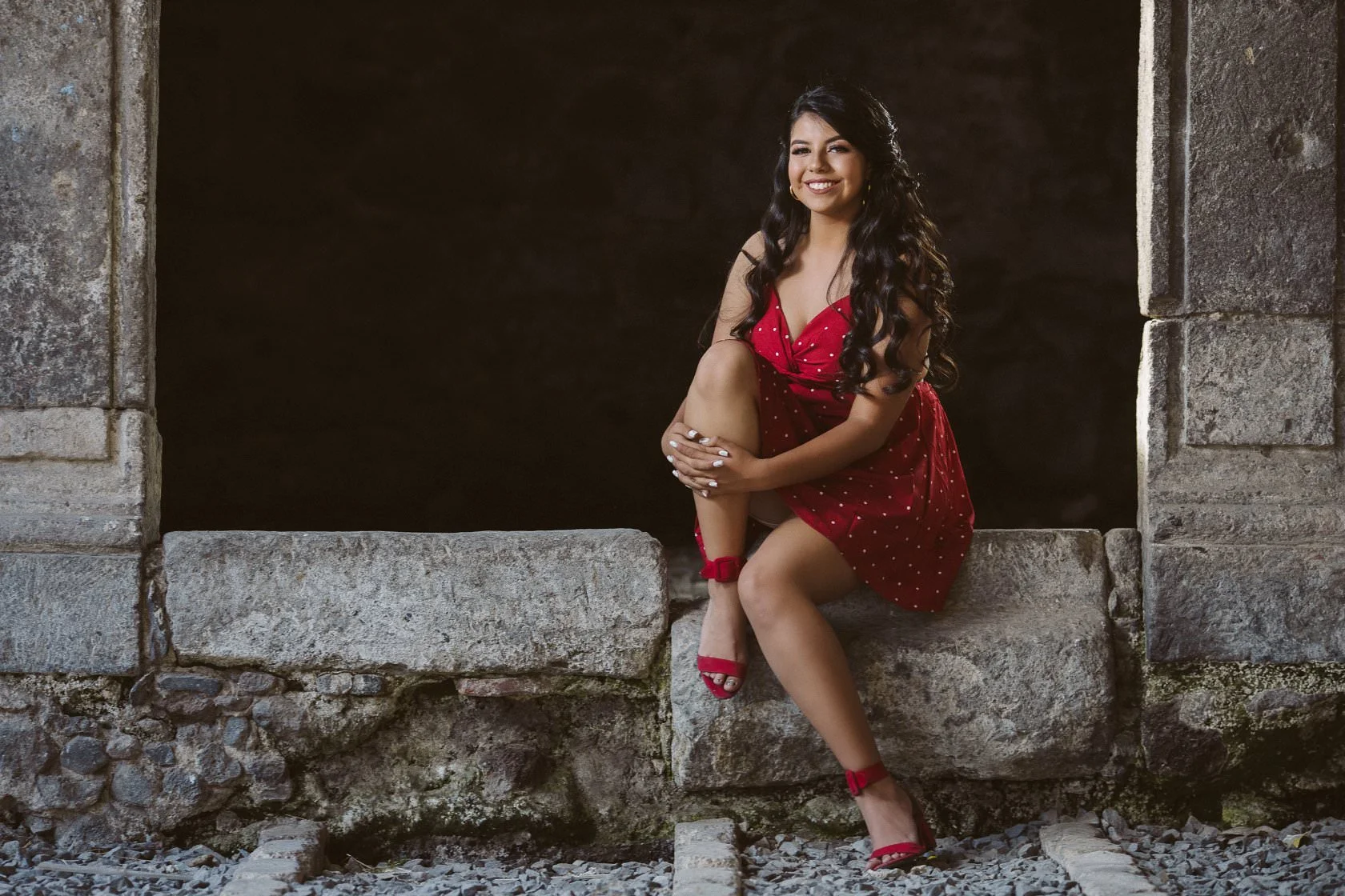 Mujer joven con vestido rojo sentada en un marco de piedra.