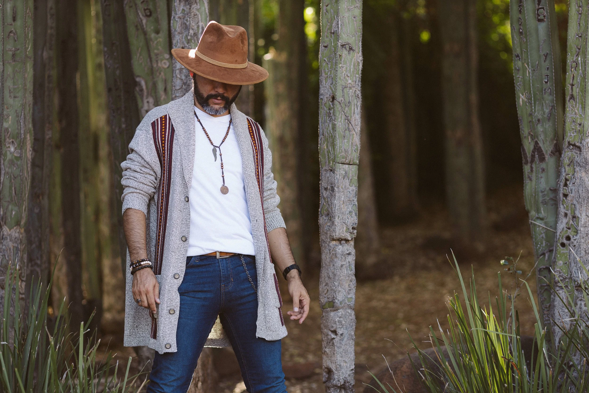 Hombre con sombrero marrón y suéter gris en el bosque.