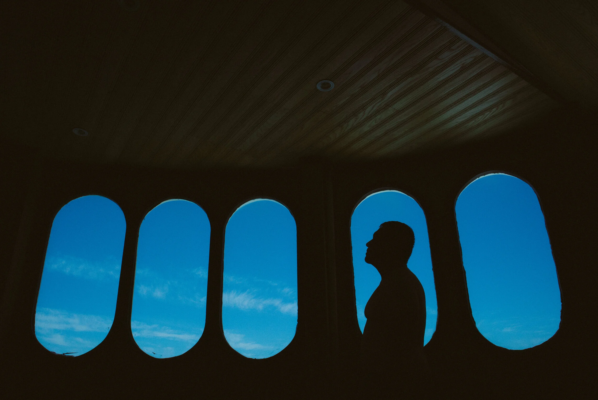 Silueta del fotógrafo JuanMa Pineda frente a una serie de ventanas con vista al cielo azul.