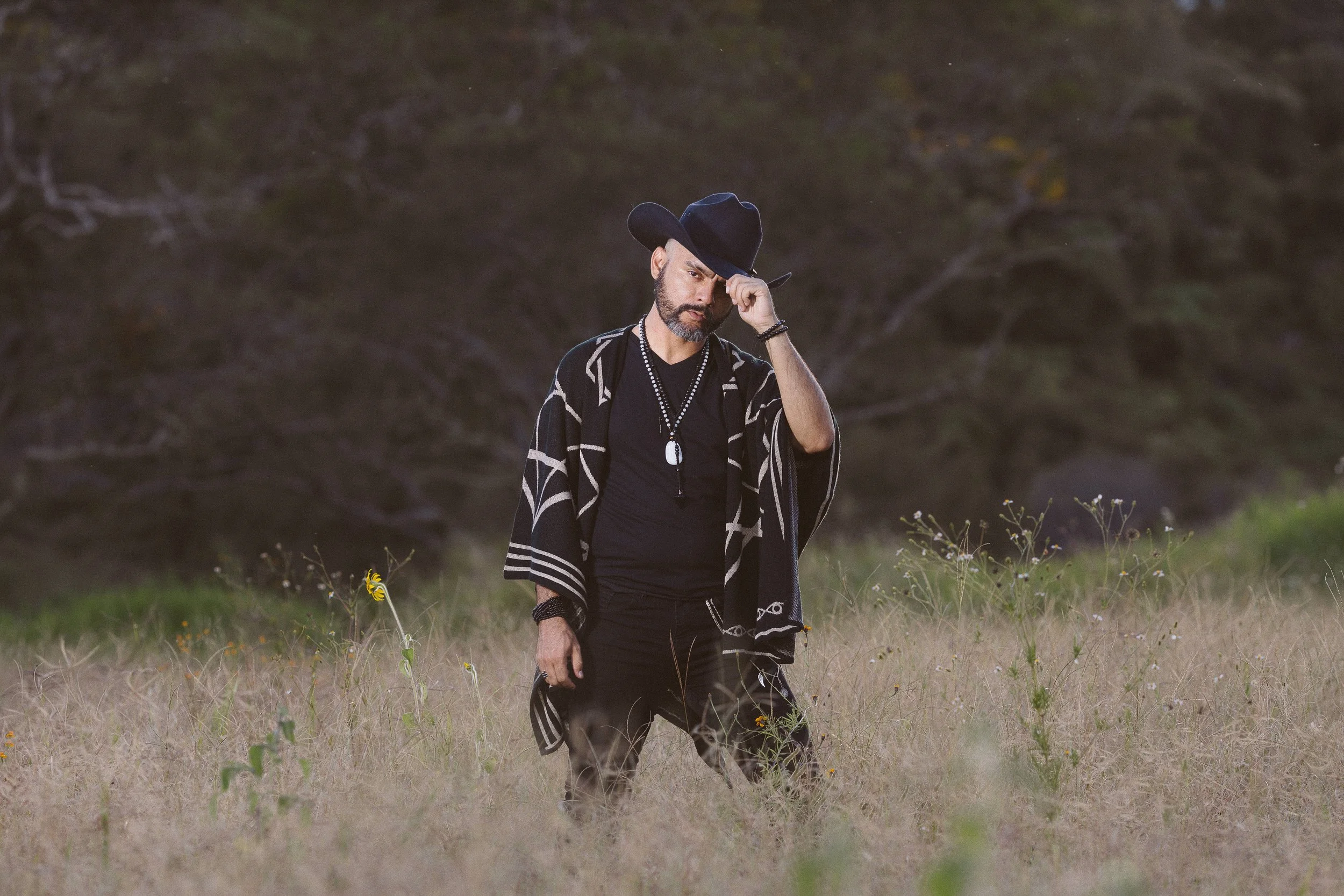 Hombre con sombrero negro y poncho en campo salvaje.