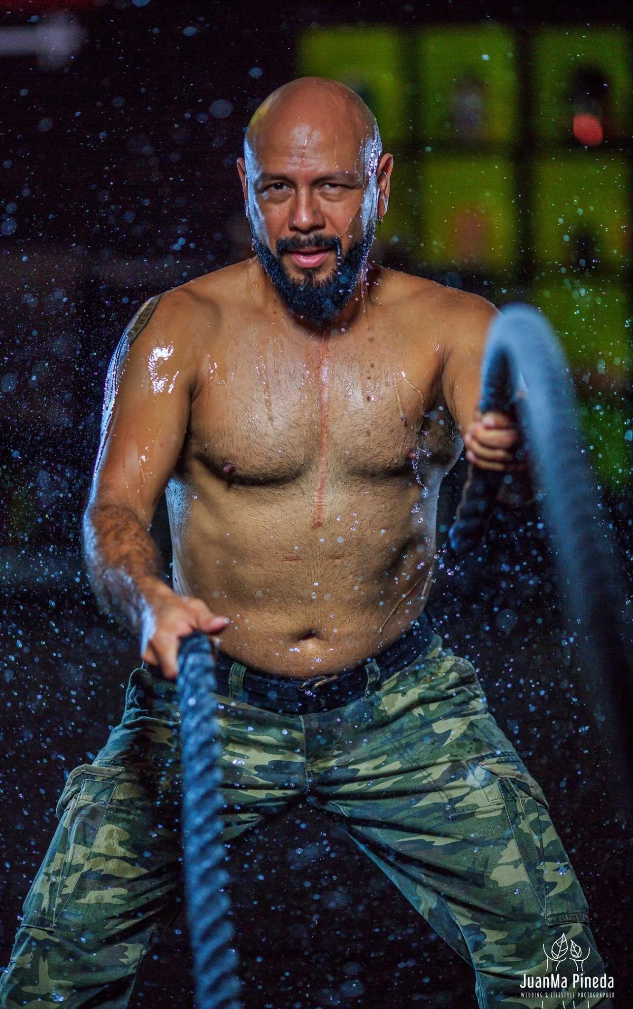 Hombre en entrenamiento usando cuerdas, mojado, lleva pantalones de camuflaje.