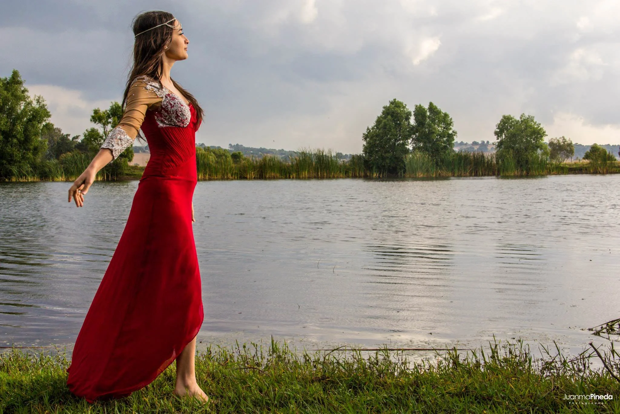 Mujer con vestido rojo cerca de un lago en un entorno natural.