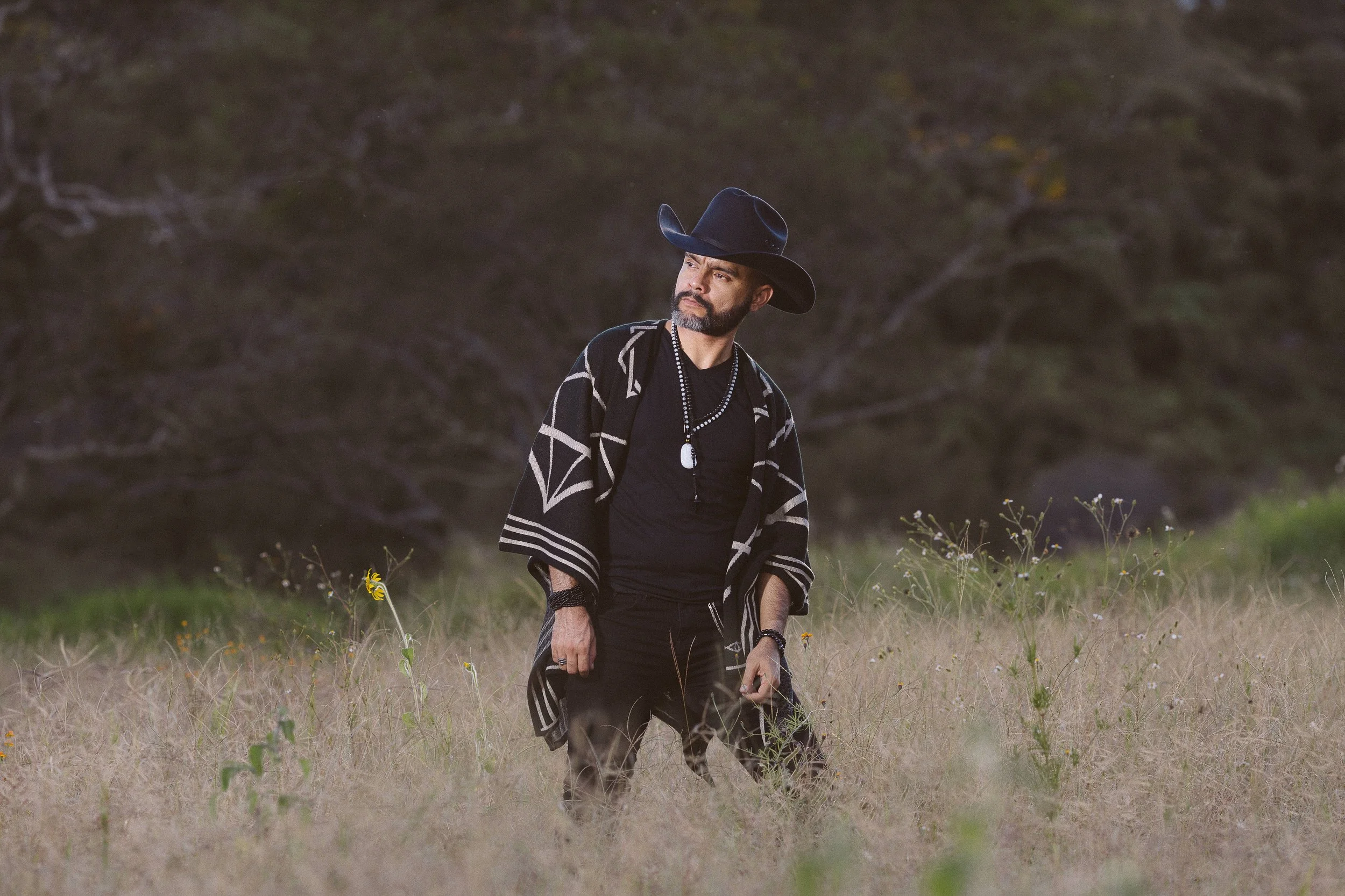 Hombre con sombrero vaquero y poncho en un campo de hierba.