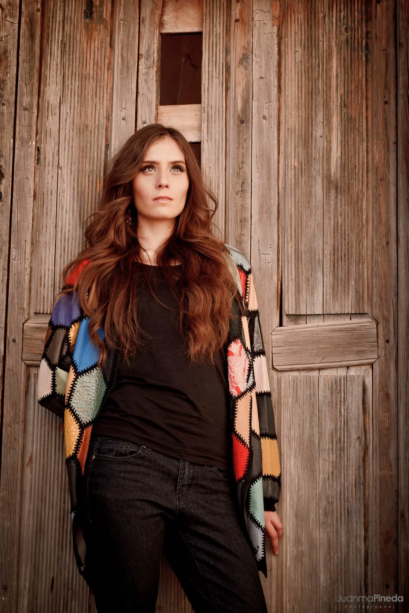 Mujer con cabello largo y suelto, vistiendo un suéter de colores, frente a una puerta de madera envejecida.