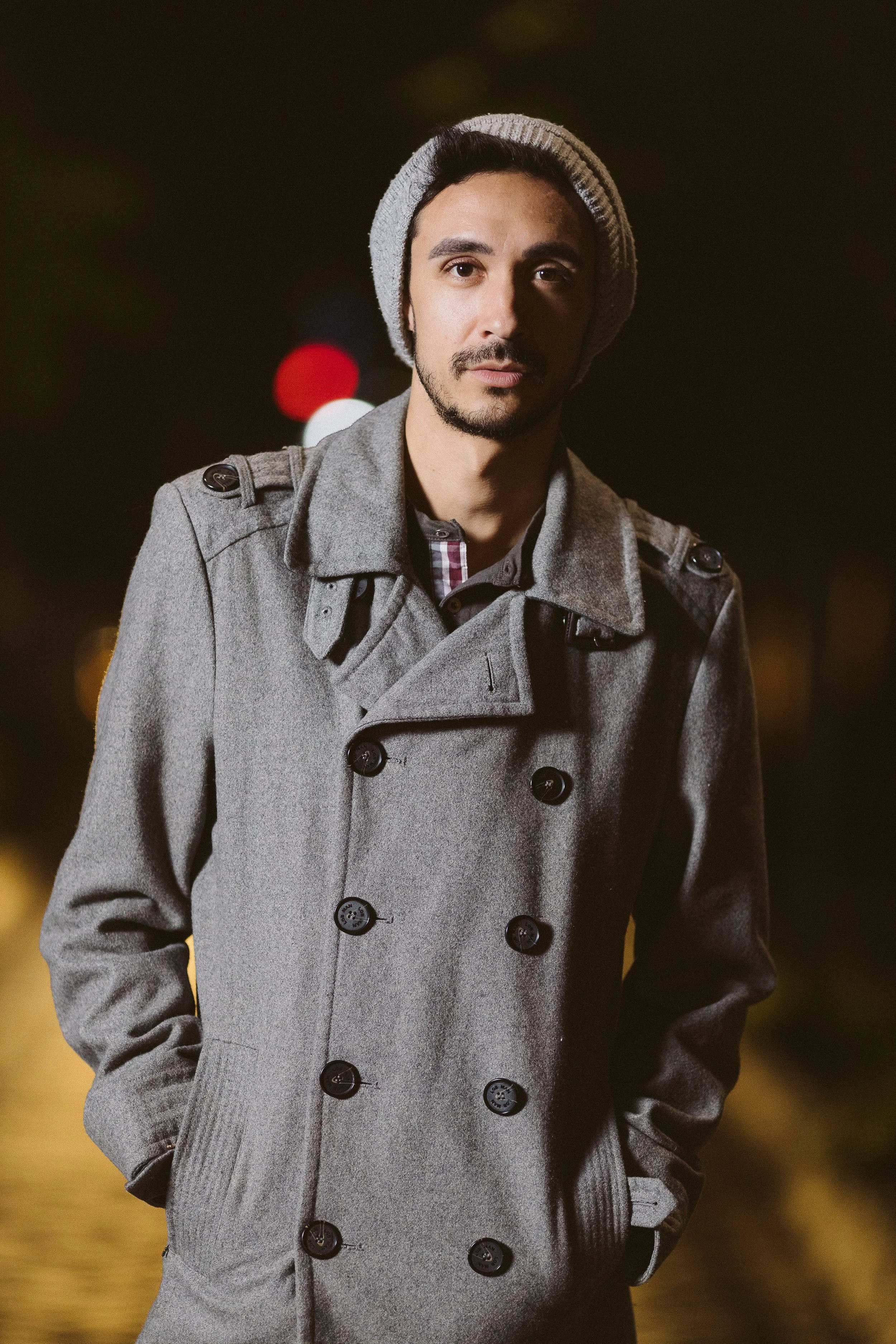 Hombre con abrigo gris y gorro de lana, de pie al aire libre por la noche.
