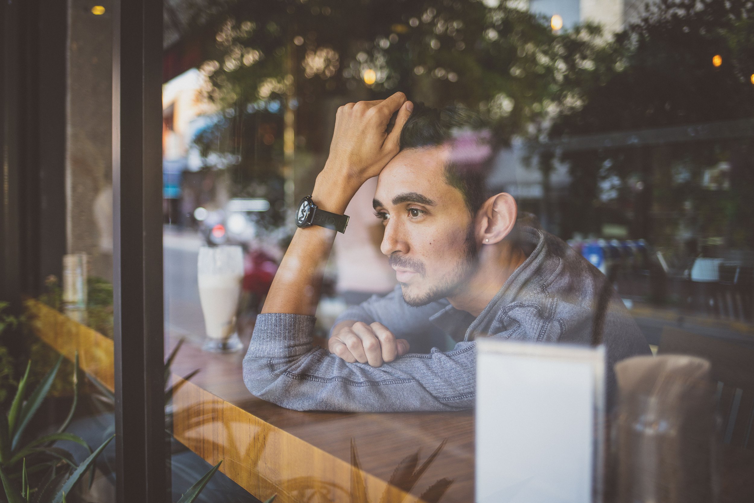 Hombre pensativo sentado en una cafetería, mirando por la ventana.