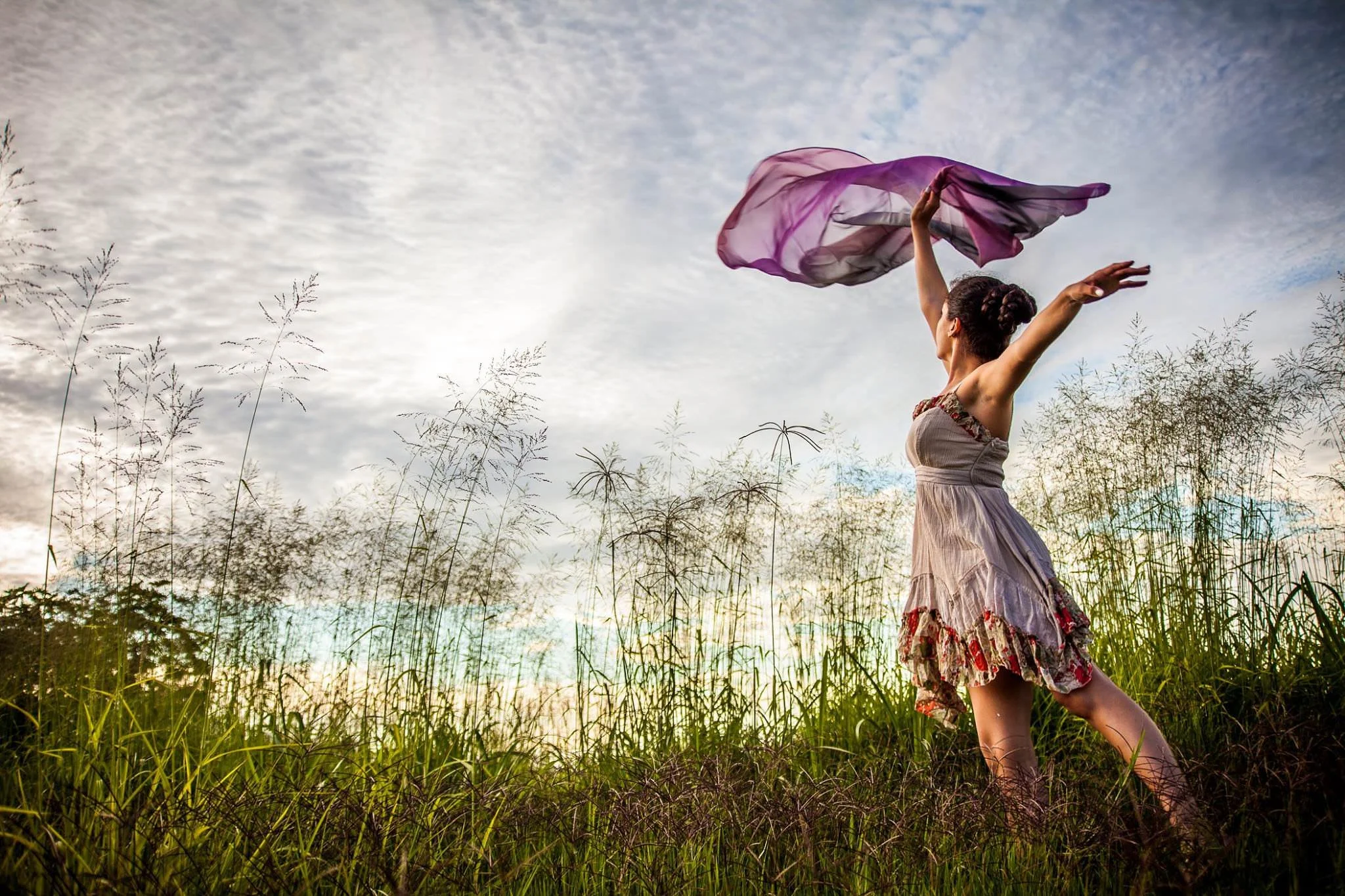 Mujer bailando en un campo con un pañuelo morado al aire.