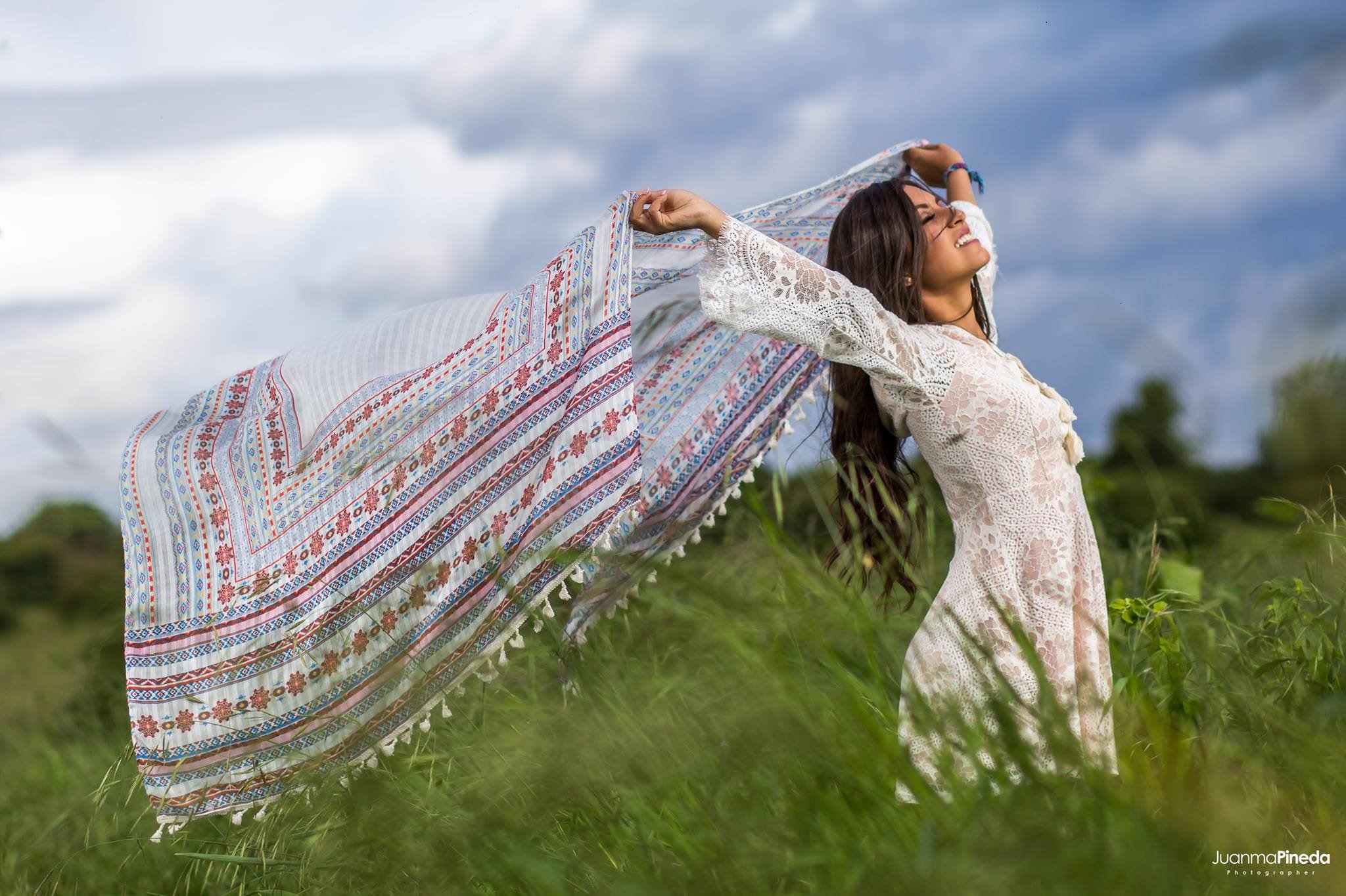 Mujer sonriendo con vestido blanco y pañuelo en un campo verde.