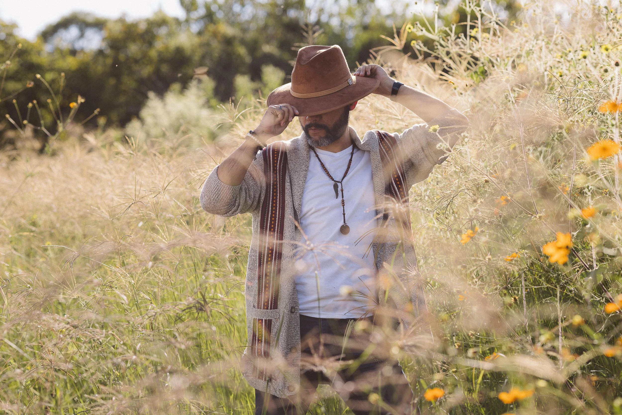 Hombre con sombrero marrón en campo con flores y hierba alta.