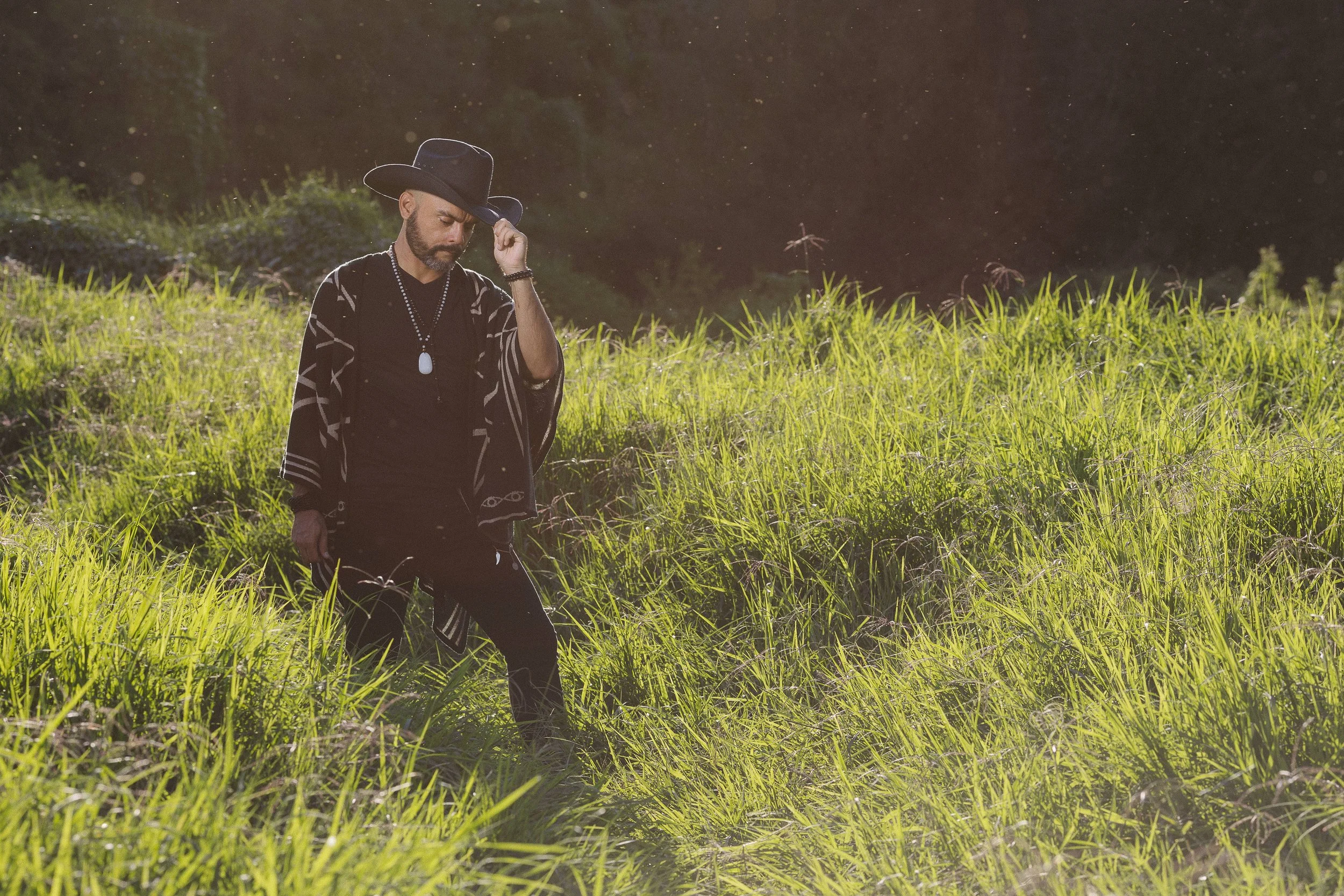 Hombre con sombrero negro caminando en un campo verde iluminado por el sol.