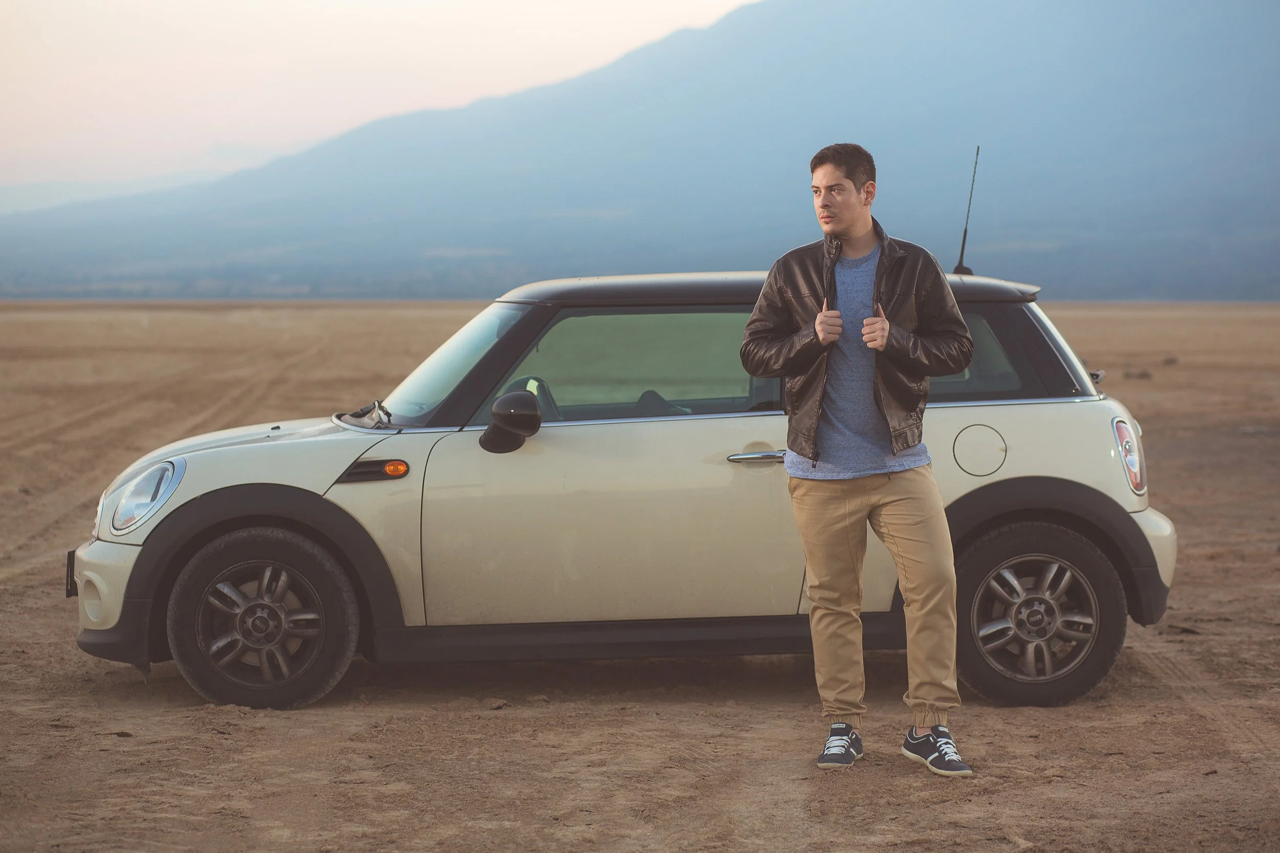 Hombre de pie junto a un auto Mini Cooper en un campo abierto.