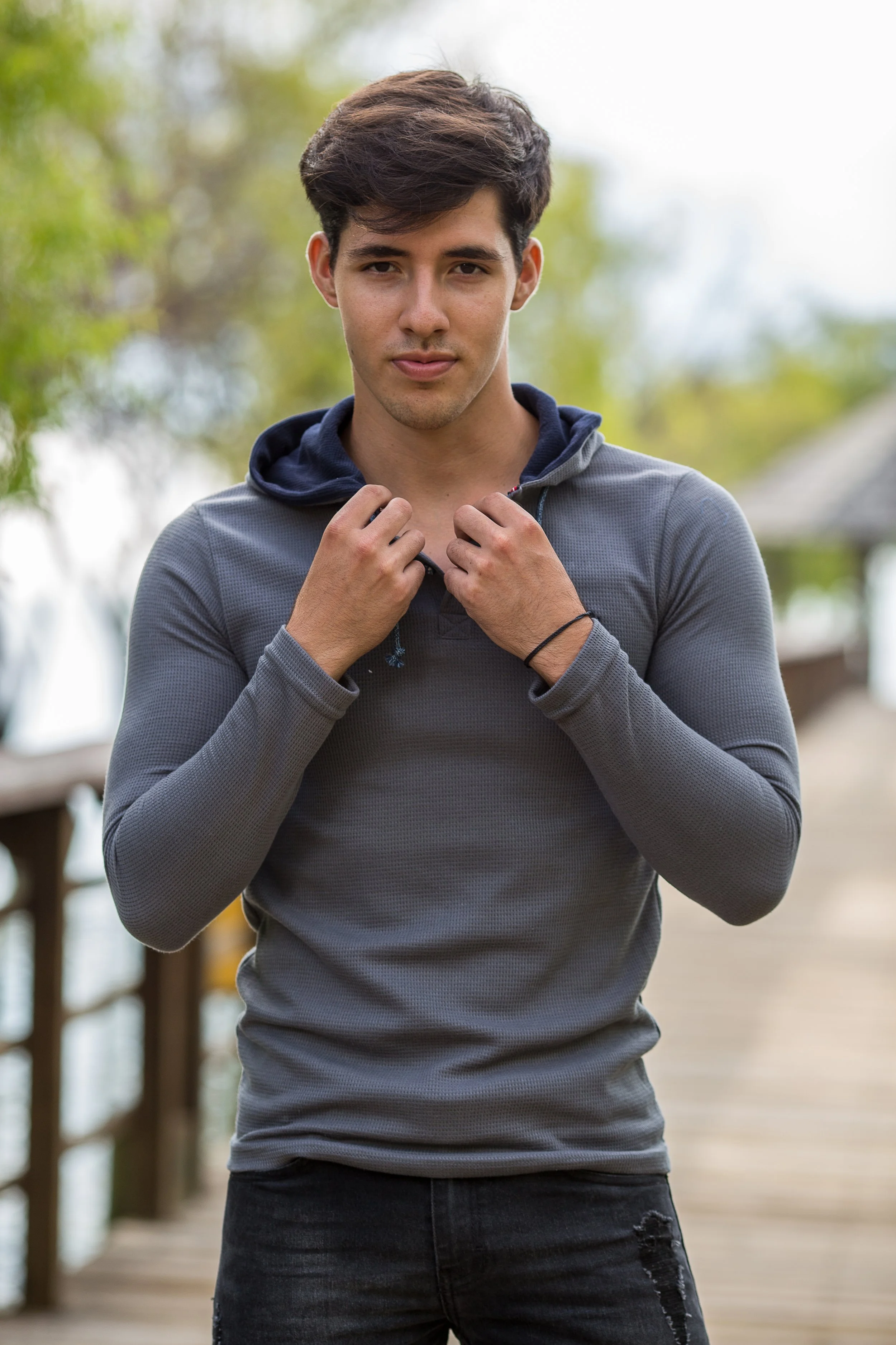 Joven posando con sudadera gris en un puente al aire libre.