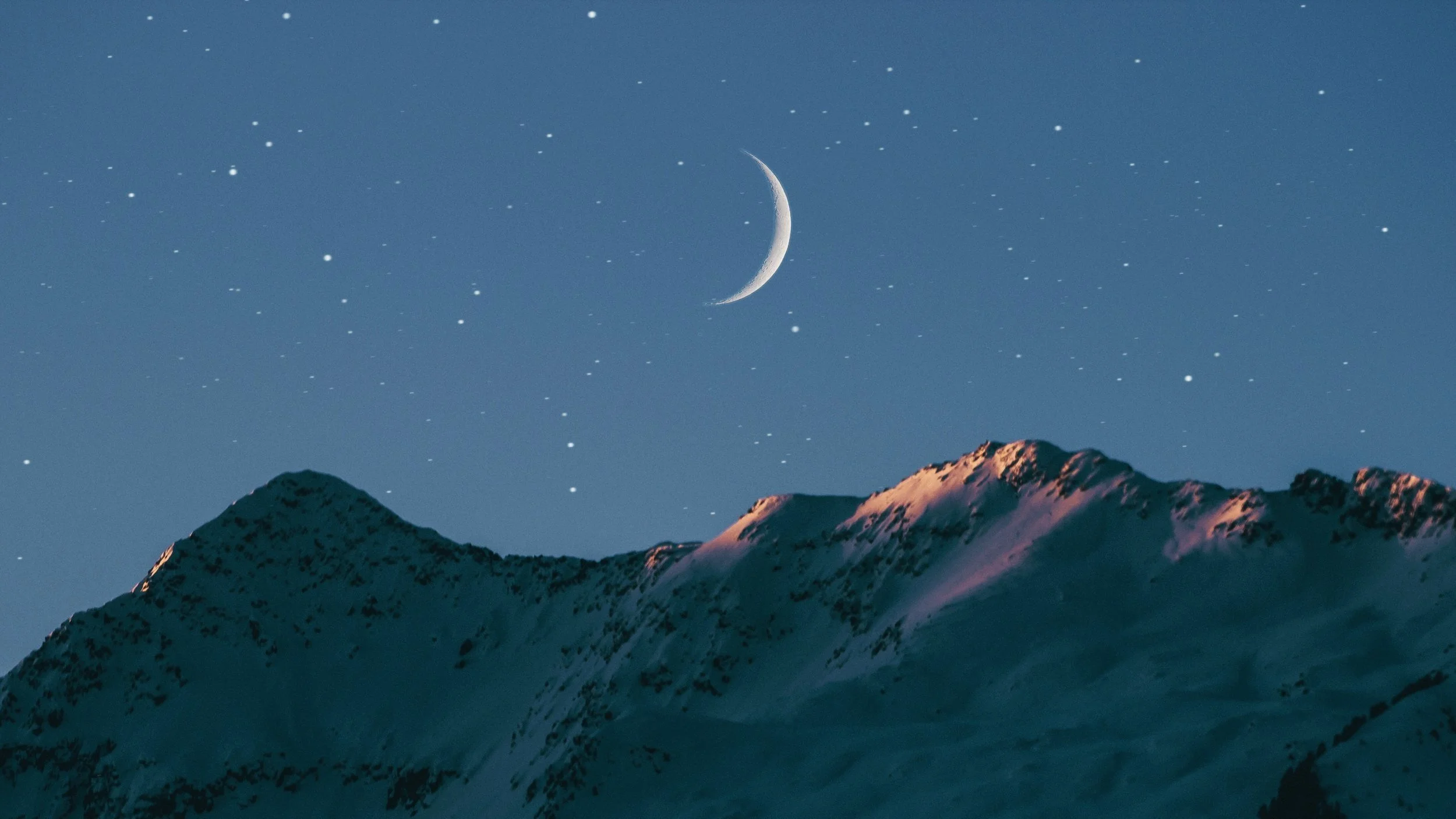 Snow-covered mountain peaks under a night sky filled with stars and a crescent moon.