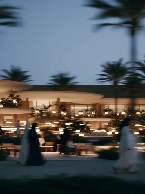 M11 · Árdh, concept image — a low curved pavilion lit at dusk among palms, figures walking past in motion blur