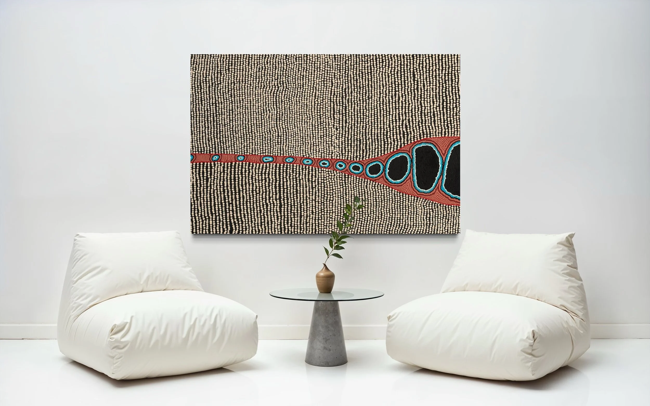 Minimalist white living room with two large, soft white bean bag chairs, a small round glass table with a potted plant, and an abstract wall art piece featuring dotted patterns and a red, black, and blue design.