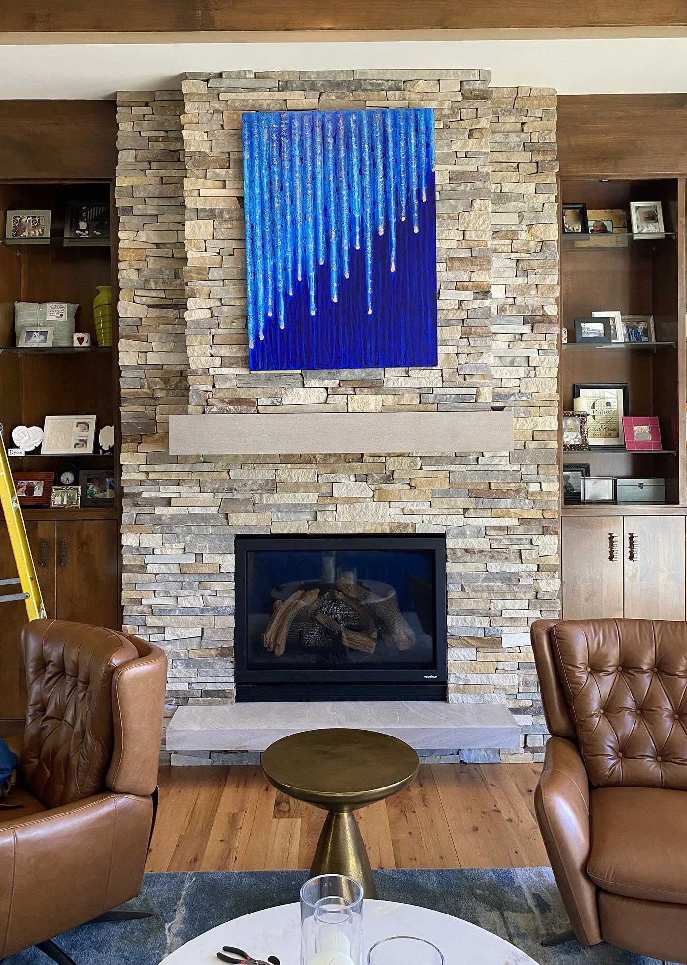 Living room with a stone fireplace, blue modern art hanging above it, and brown leather armchairs.