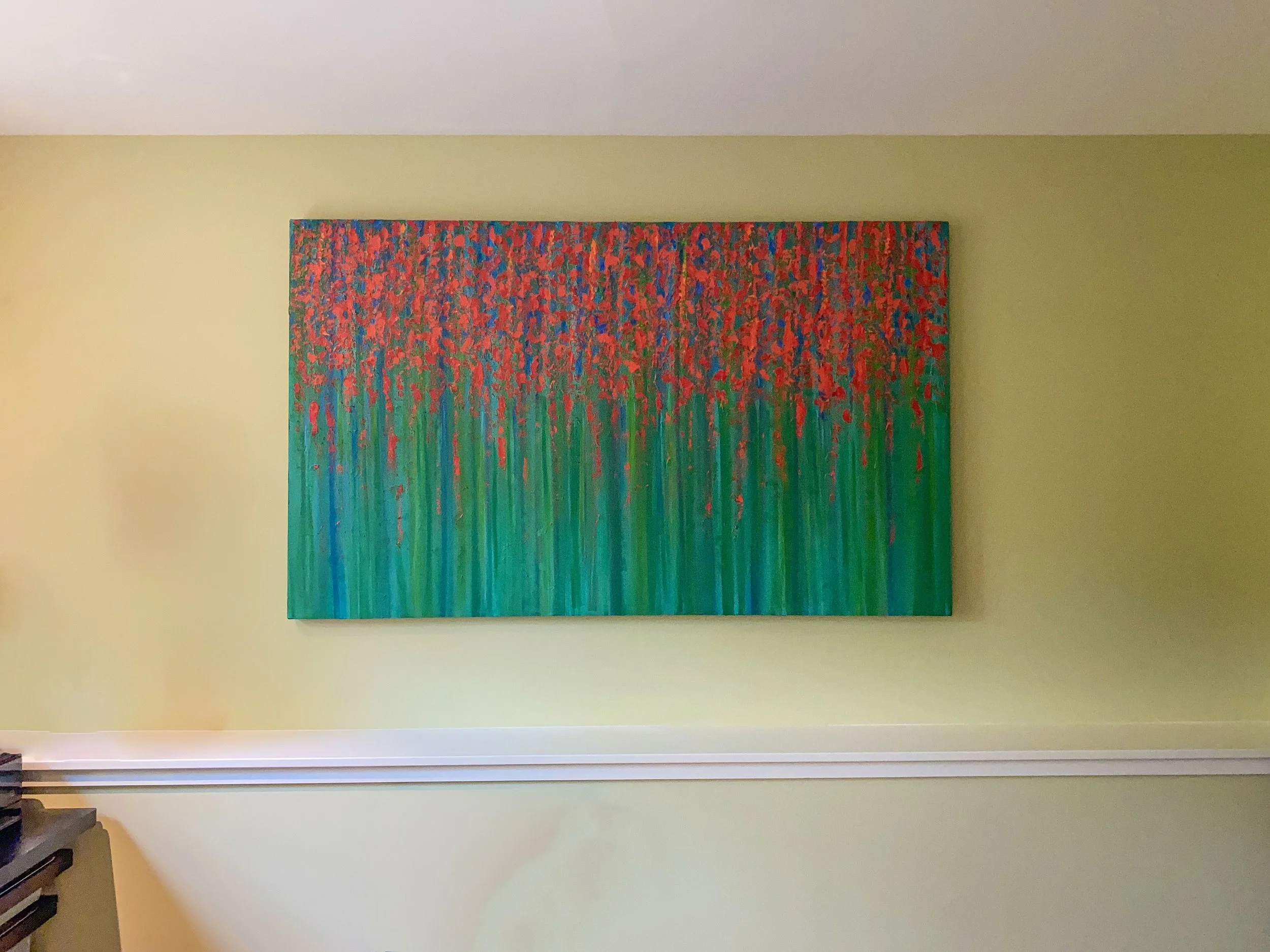 Abstract painting with red, orange, and blue dots on top of green and blue vertical stripes, hanging on a yellow wall.