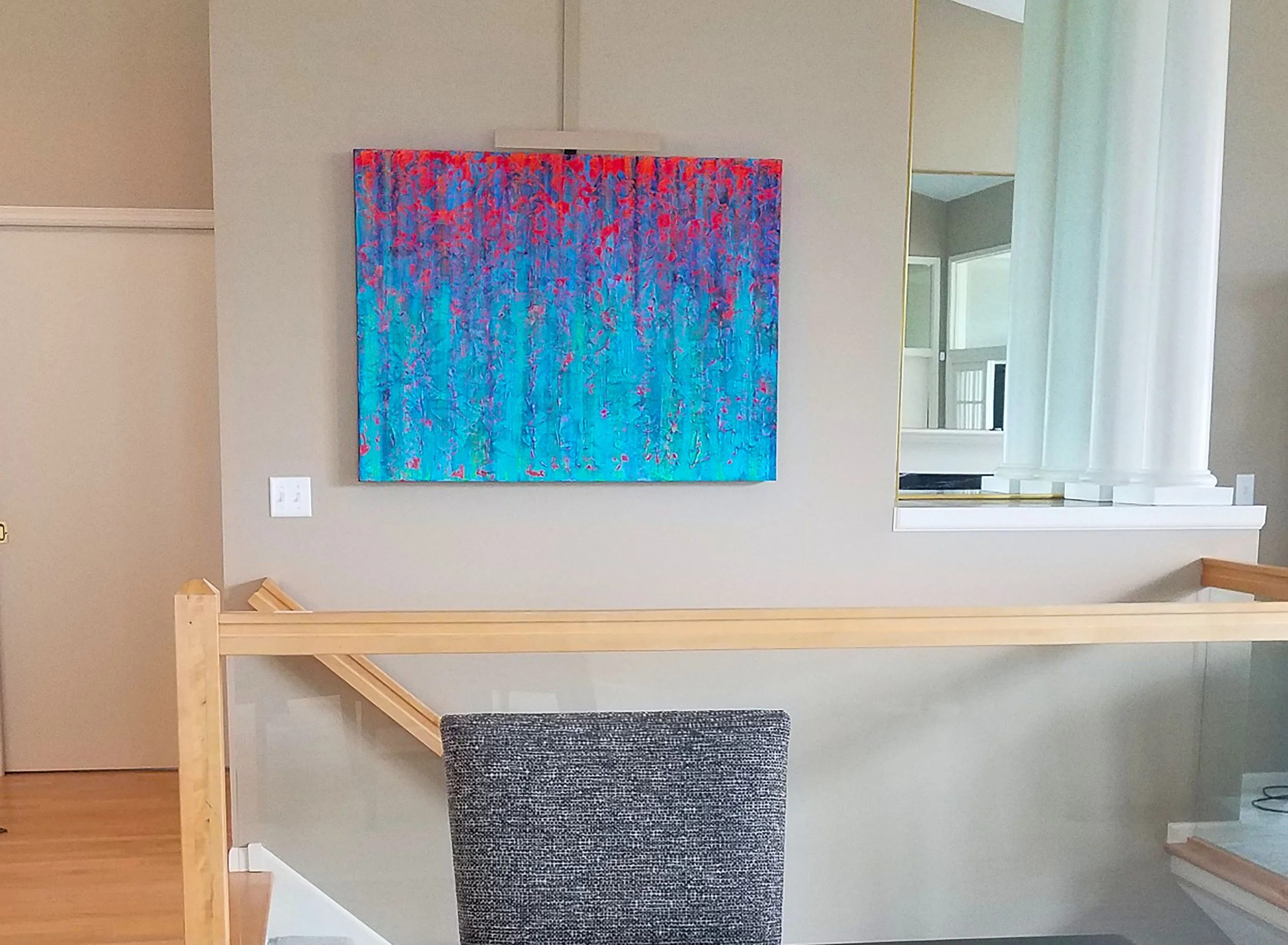 Abstract painting with blue and red colors hanging on a beige wall in a room with large windows and white columns.