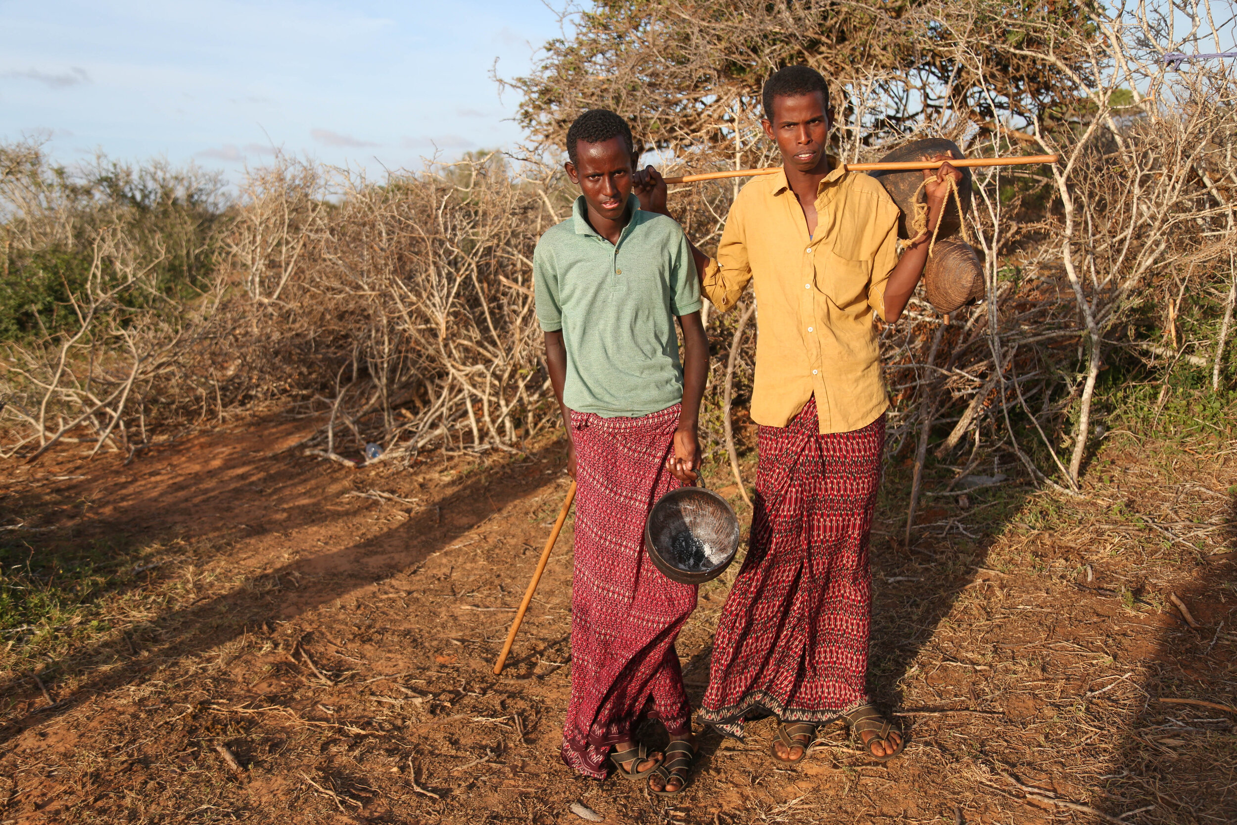 Two young camel herders holding traditional milk container made out of trees. 