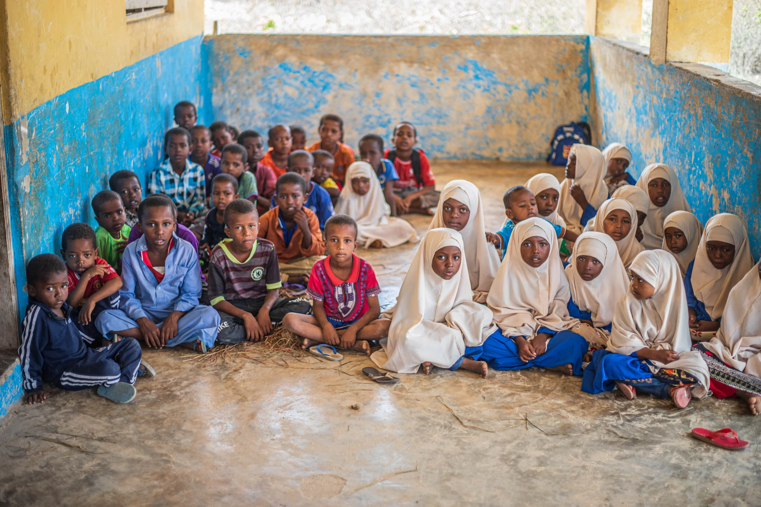 Students sit on the floor of a school in Koyama Island, Somalia, without desks or mats. Living on the isolated island, the children lack access to basic educational necessities, including desks and other essential school supplies.