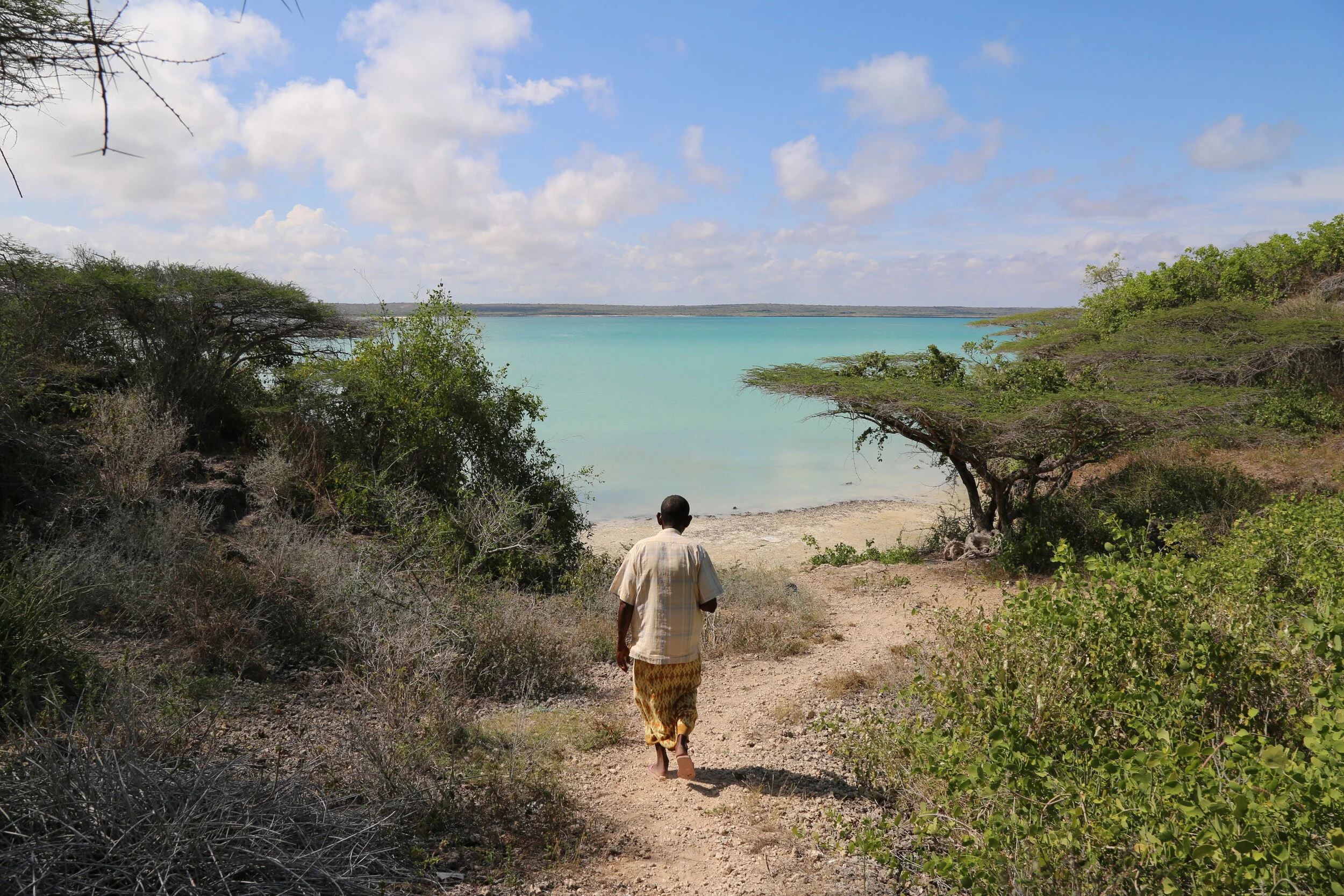 A local guide walks along a dirt path on Koyama Island in Somalia’s Lower Juba region, towards turquoise waters. 