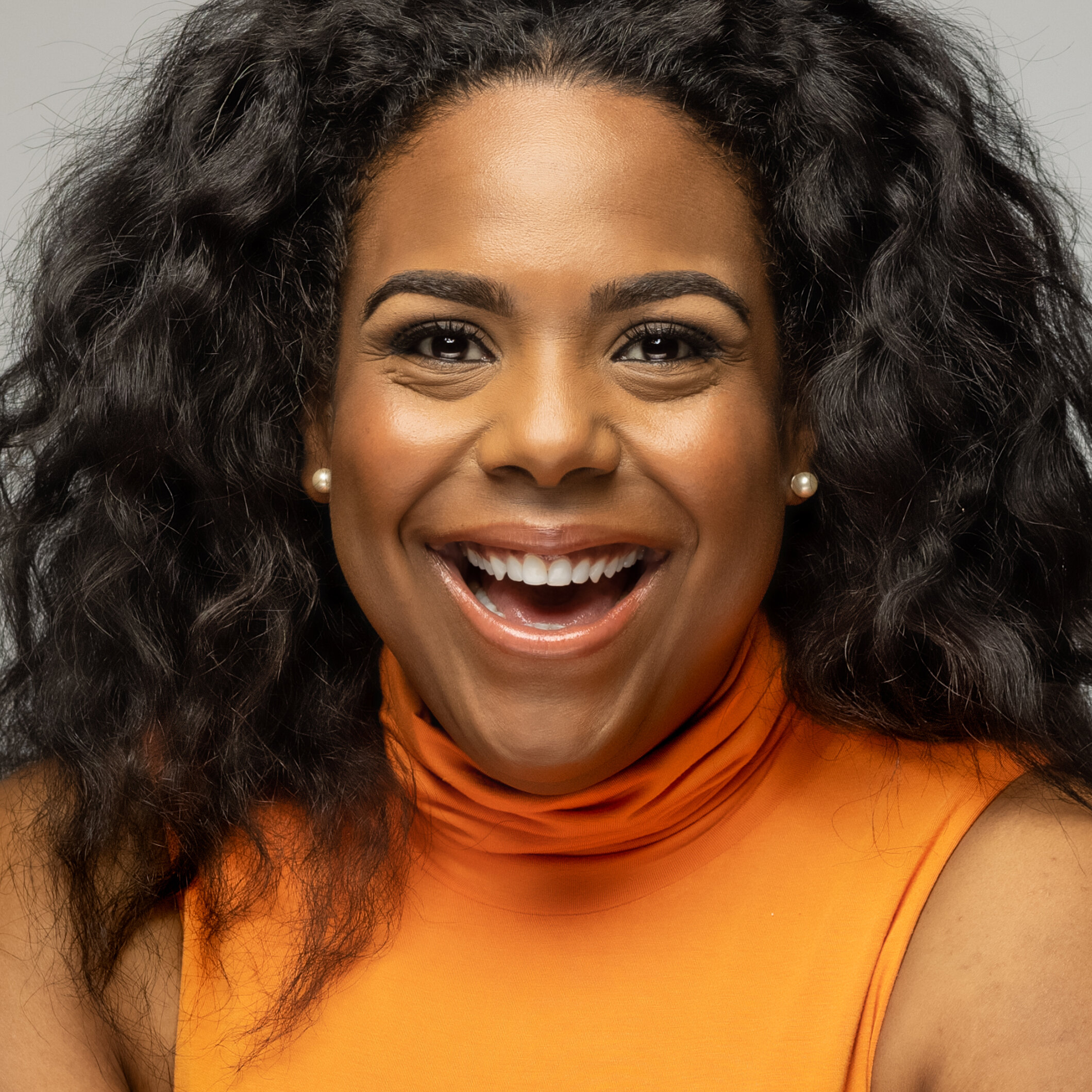 woman with long wide black hair wearing orange turtleneck top lo